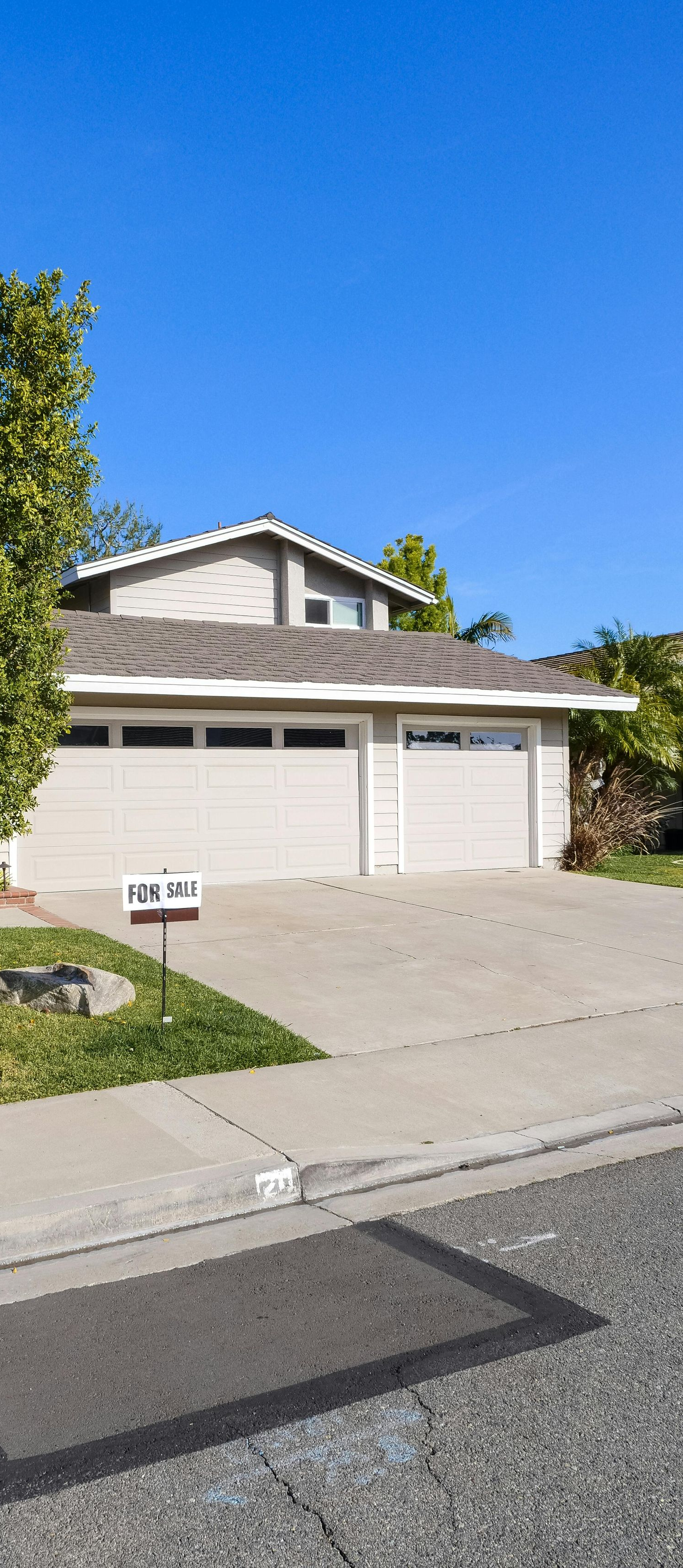 Suburban house with two-car garage, tree, and driveway under a clear blue sky