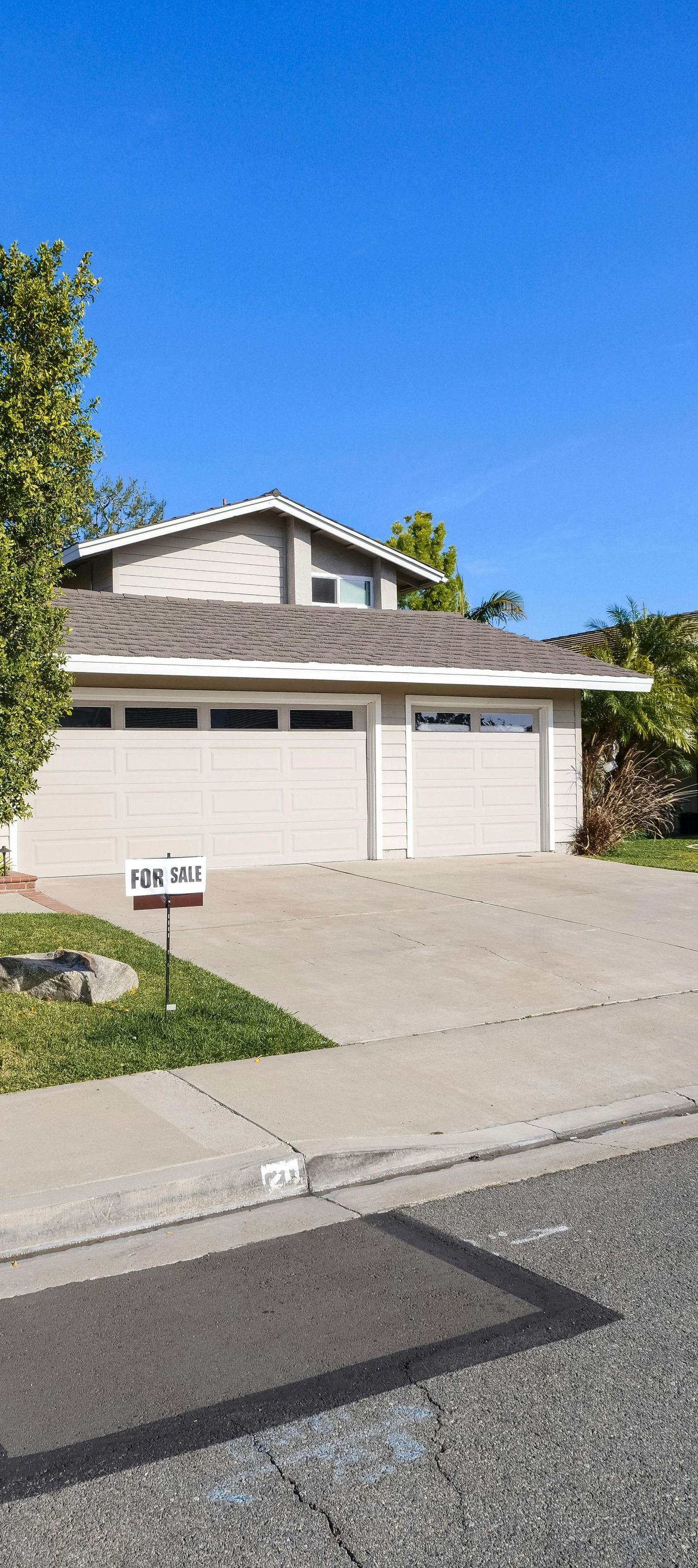 Suburban house with two-car garage, tree, and driveway under a clear blue sky