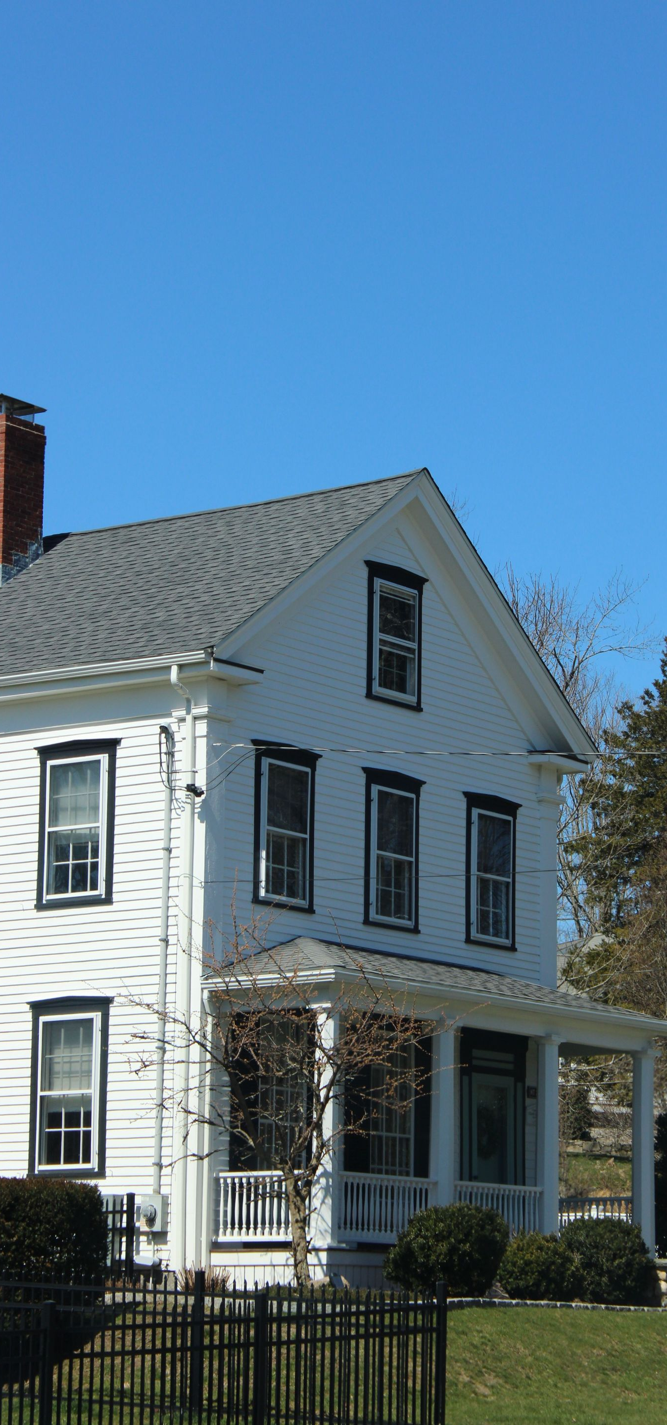 White two-story house with black shutters and a brick chimney against a blue sky