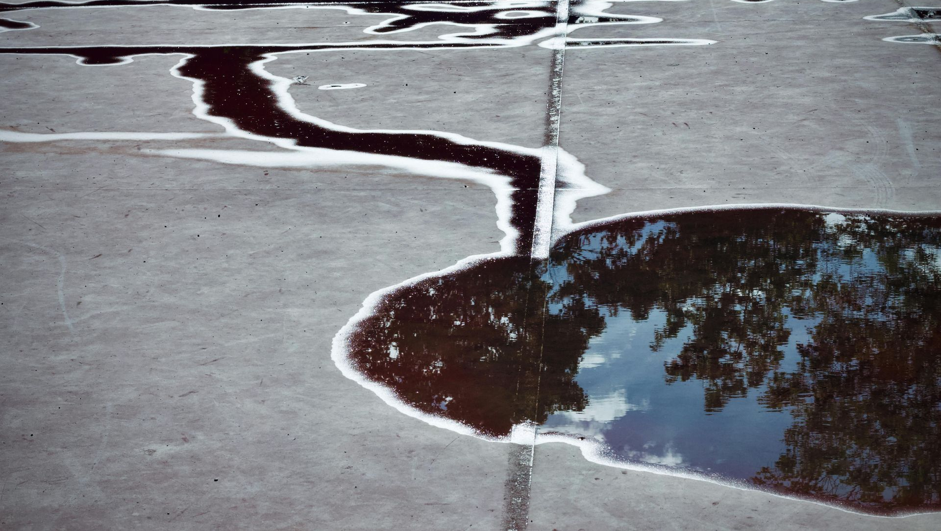 Cracked pavement with a narrow stream of water flowing toward a reflective puddle