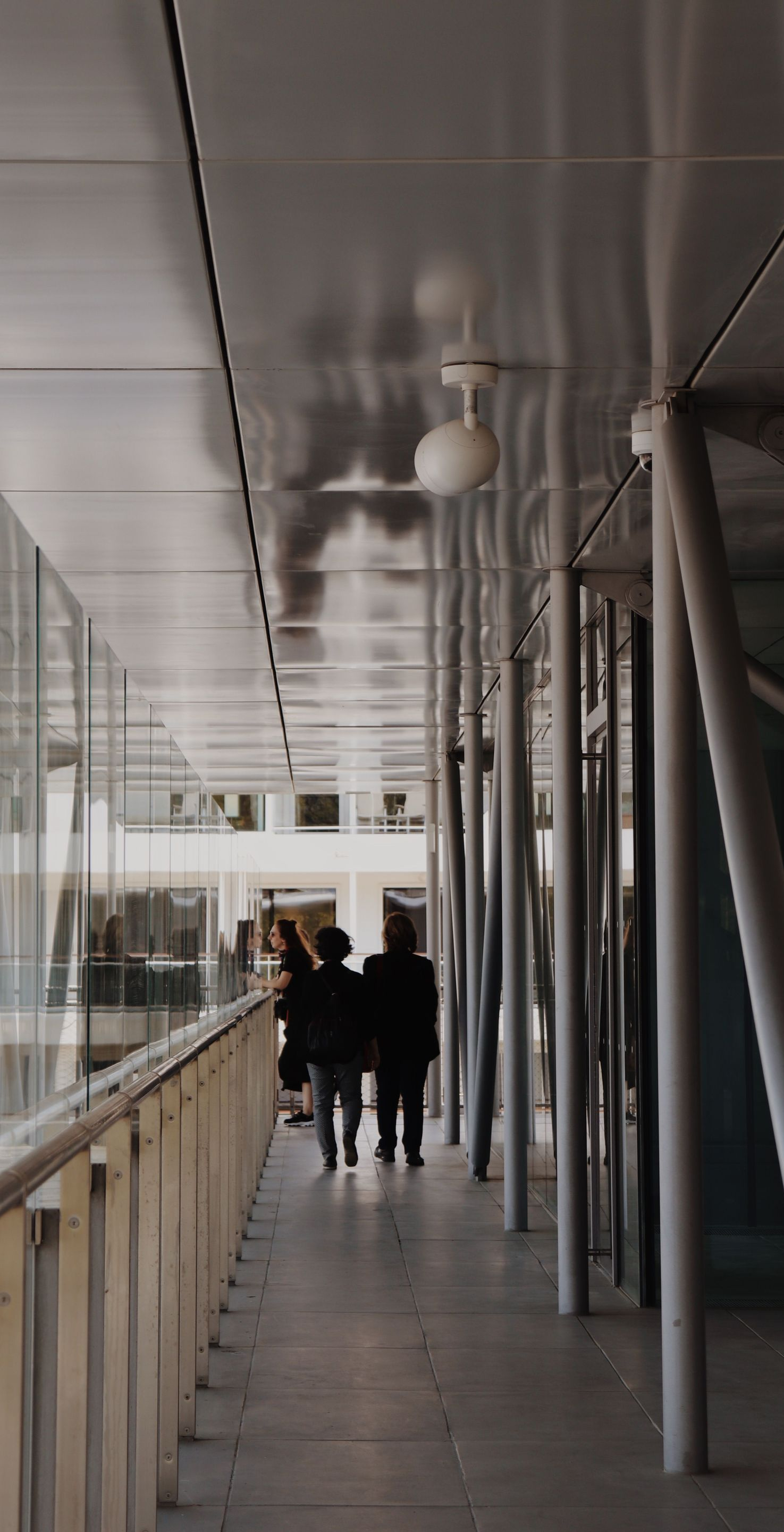 Covered walkway with metal columns and railing, with several people walking away in the distance