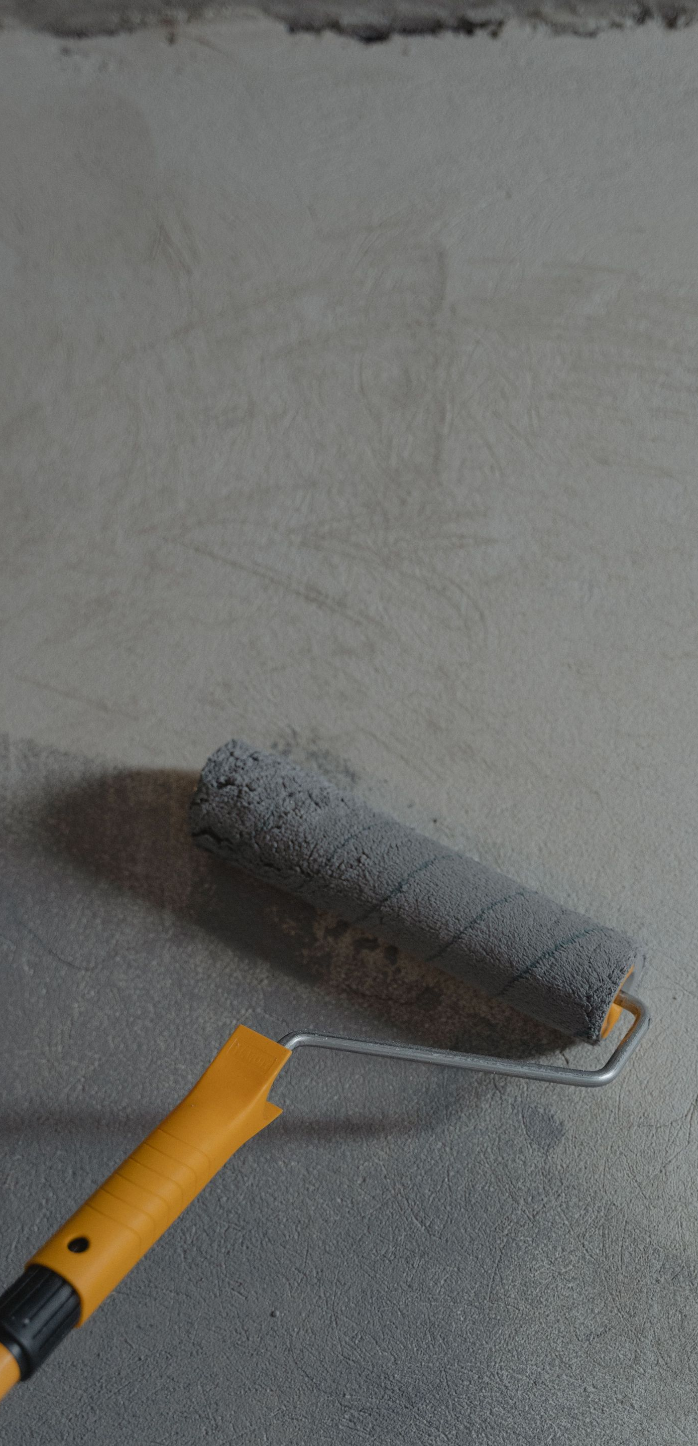 Paint roller applying gray paint to a wall with a yellow handle