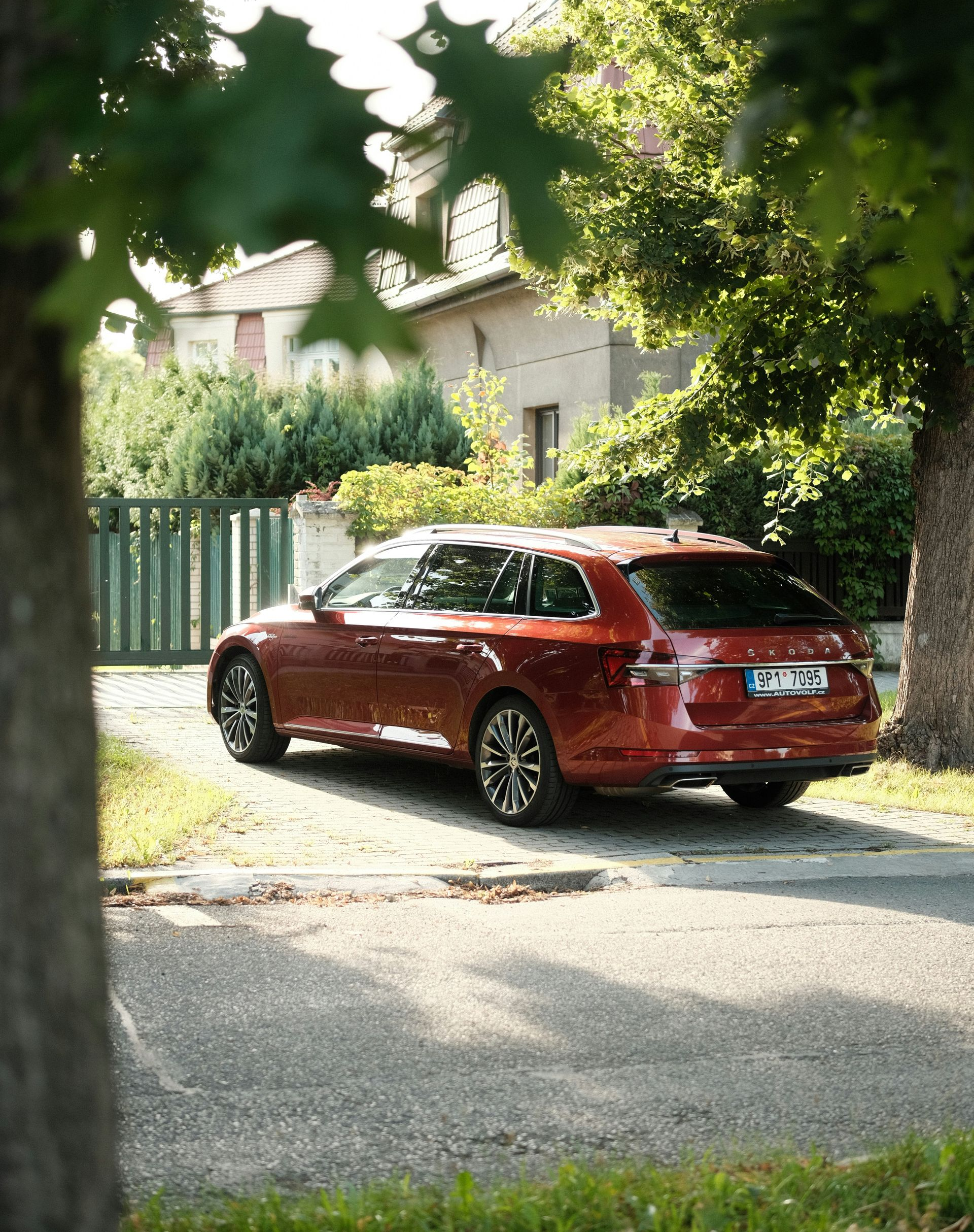 Red station wagon parked on a driveway near a house and trees.
