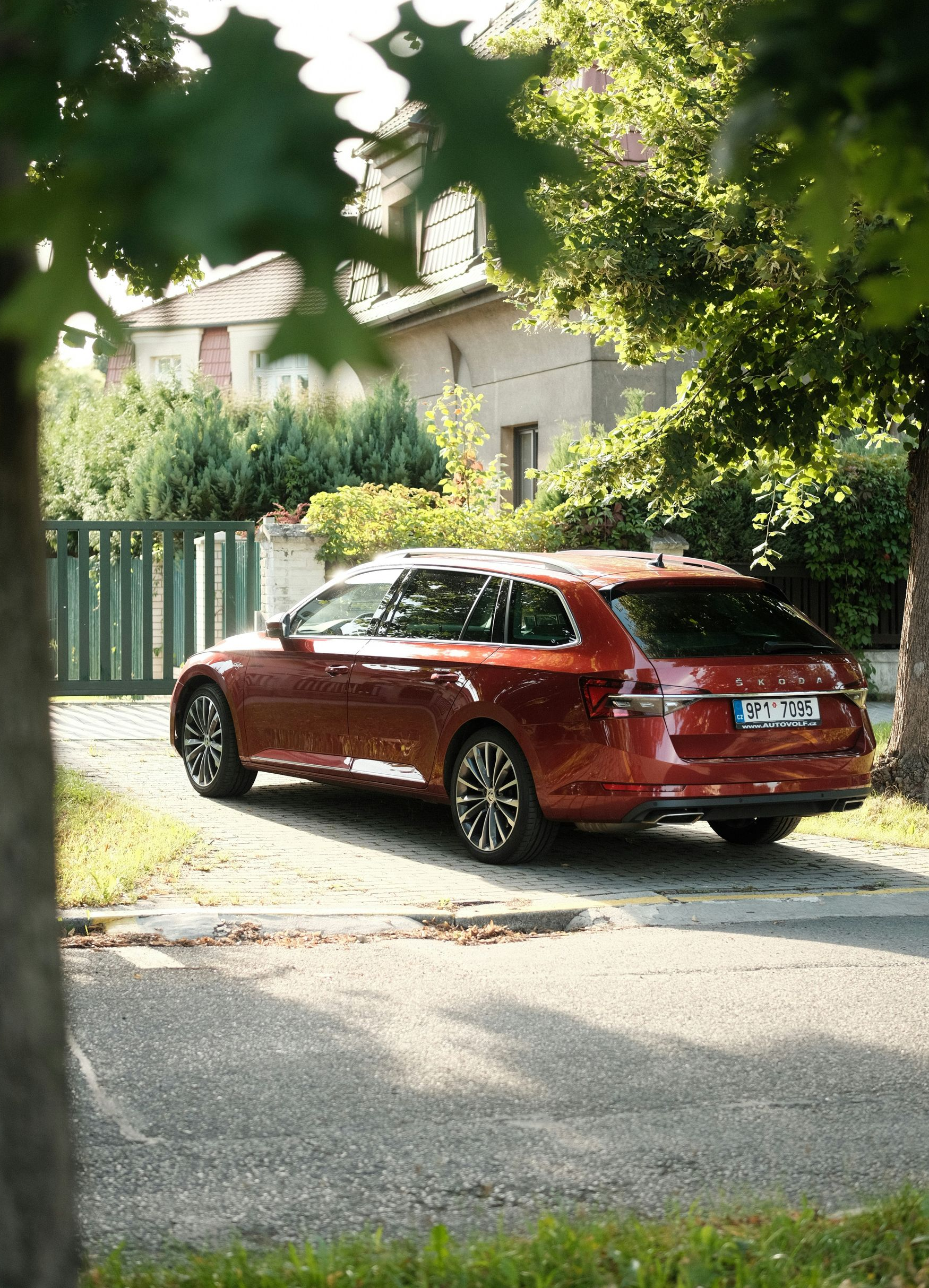 Red station wagon parked on a driveway near a house and trees.