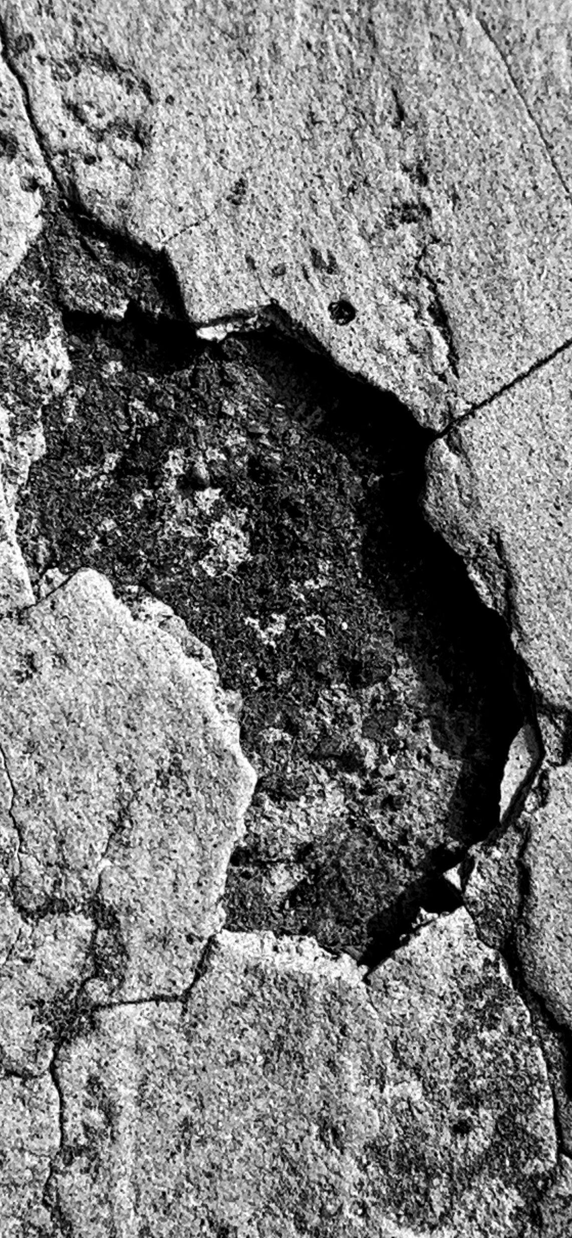 Close-up of a cracked concrete surface with a large missing hole in the center