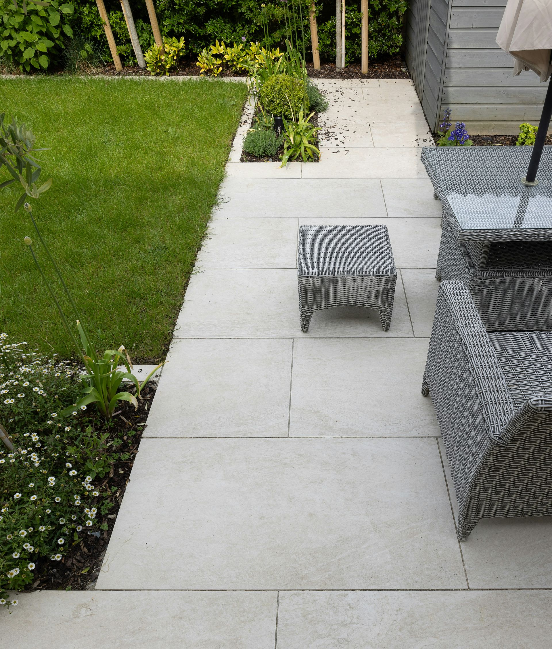 Concrete patio walkway beside a green lawn, with wicker outdoor furniture and a small ottoman.