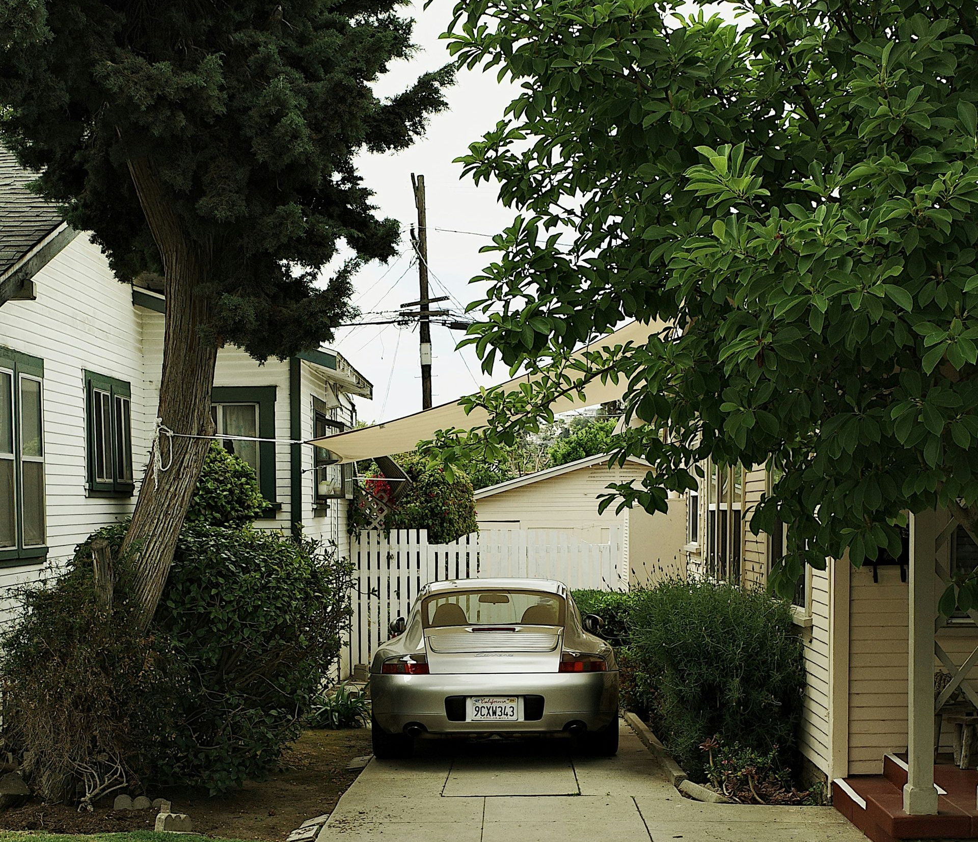Silver car parked in driveway between houses and trees.