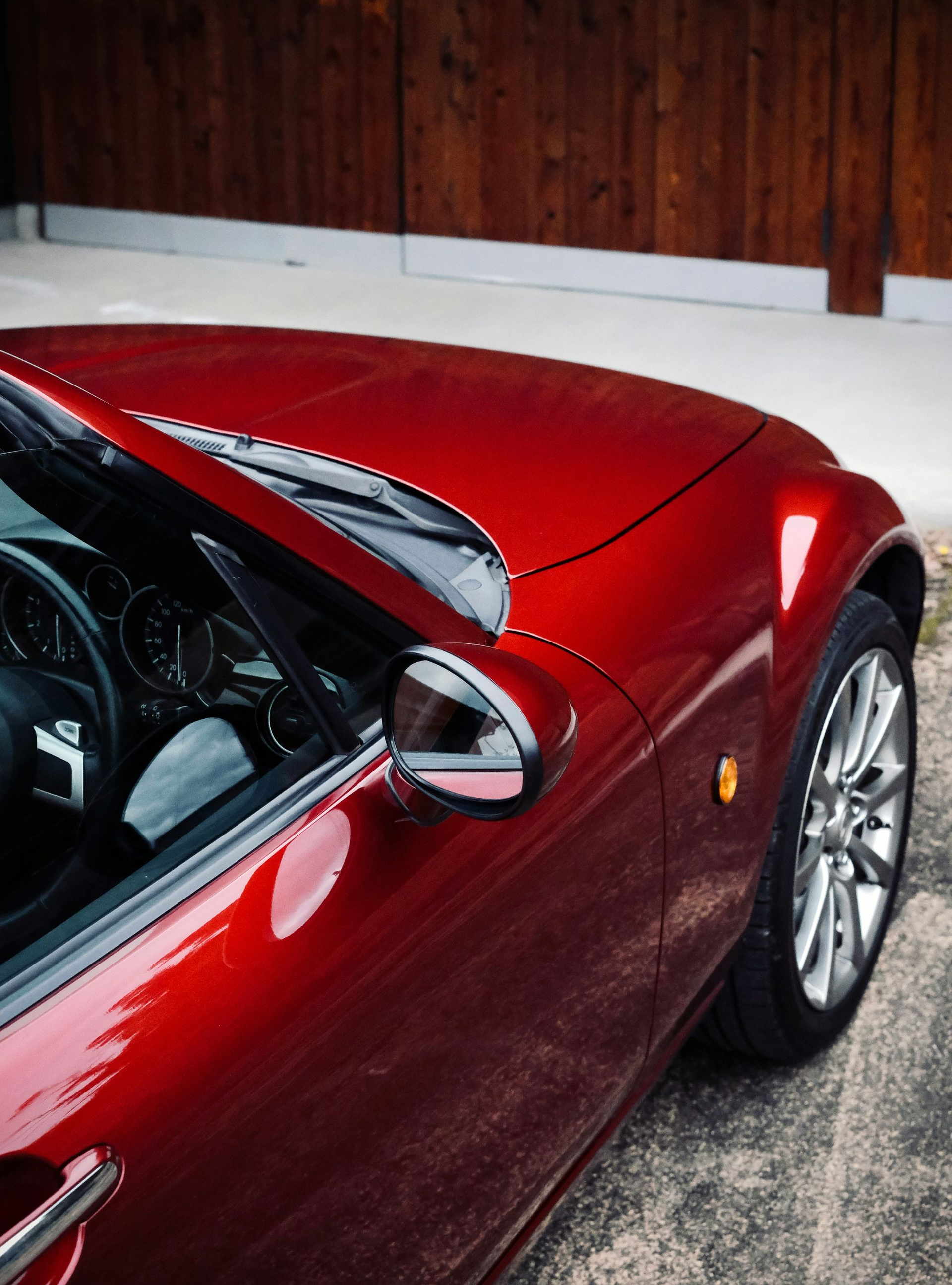 Red sports car parked next to a wooden wall. Silver wheels, glossy finish.