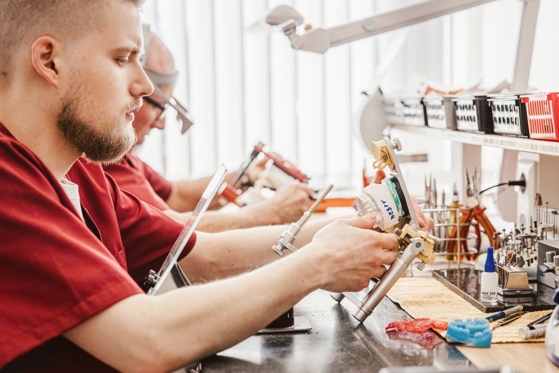 Zwei Zahntechniker in roter Arbeitskleidung saßen an einem Labortisch und konzentrierten sich auf ihre Arbeit.