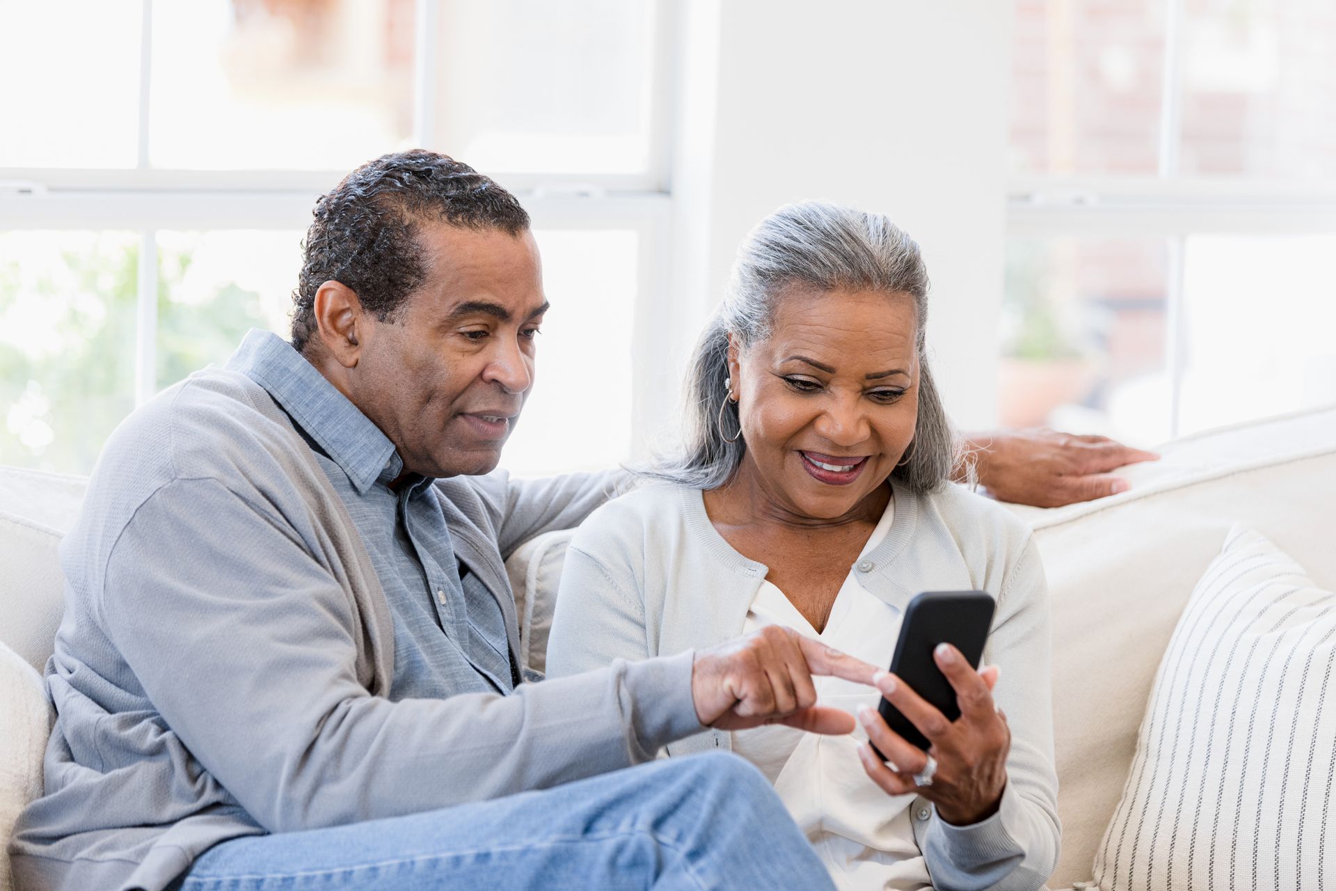 An elderly couple is sitting on a couch looking at a cell phone.