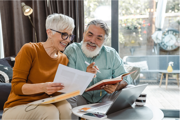 A man and a woman are sitting on a couch looking at papers and a laptop.