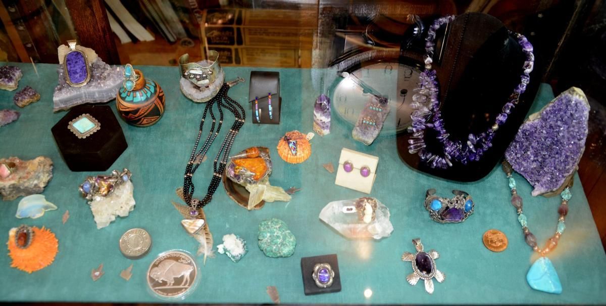 Jewelry display with gemstones, necklaces, and pendants on a teal surface in a shop window.