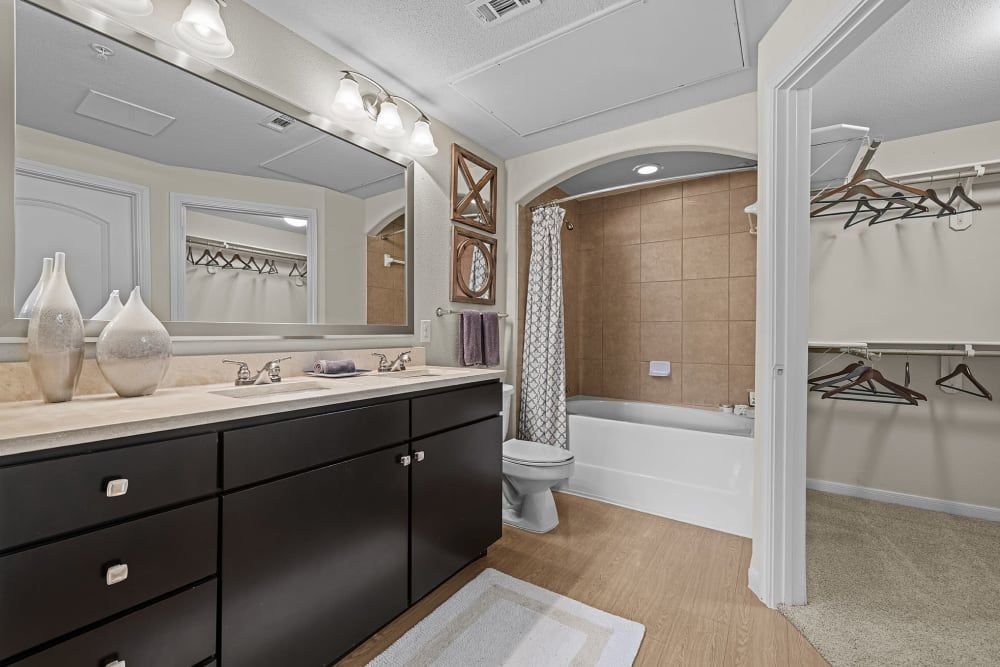 Apartment bathroom with two sinks, a toilet, and a walk-in closet at Marquis at the Reserve in Katy, TX.