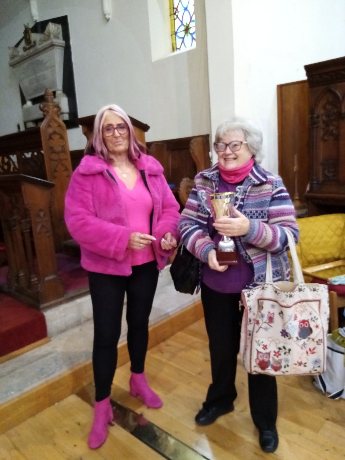 Two women standing next to each other in a church holding trophies