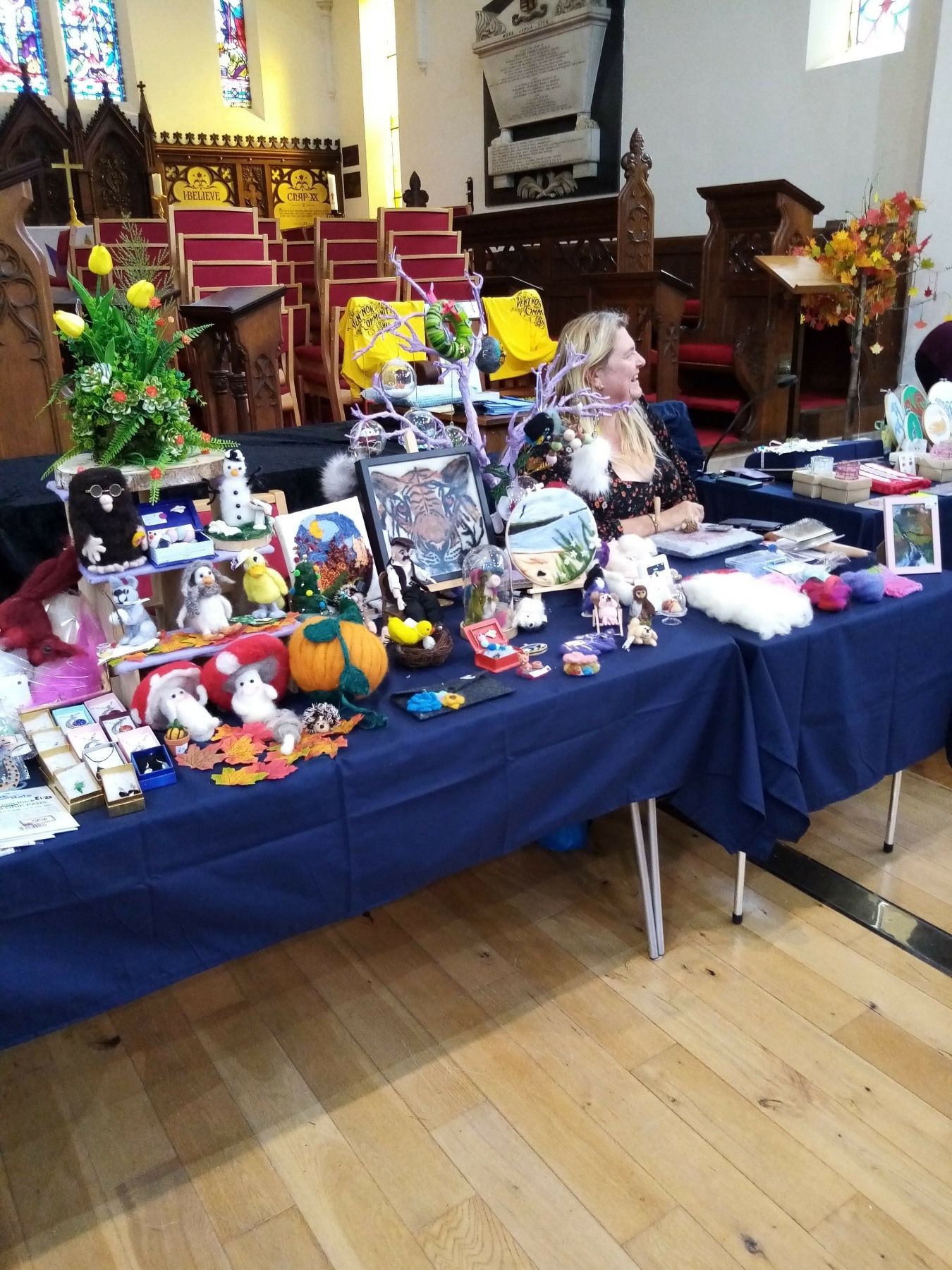 A woman is sitting at a table in a church with lots of items on it.