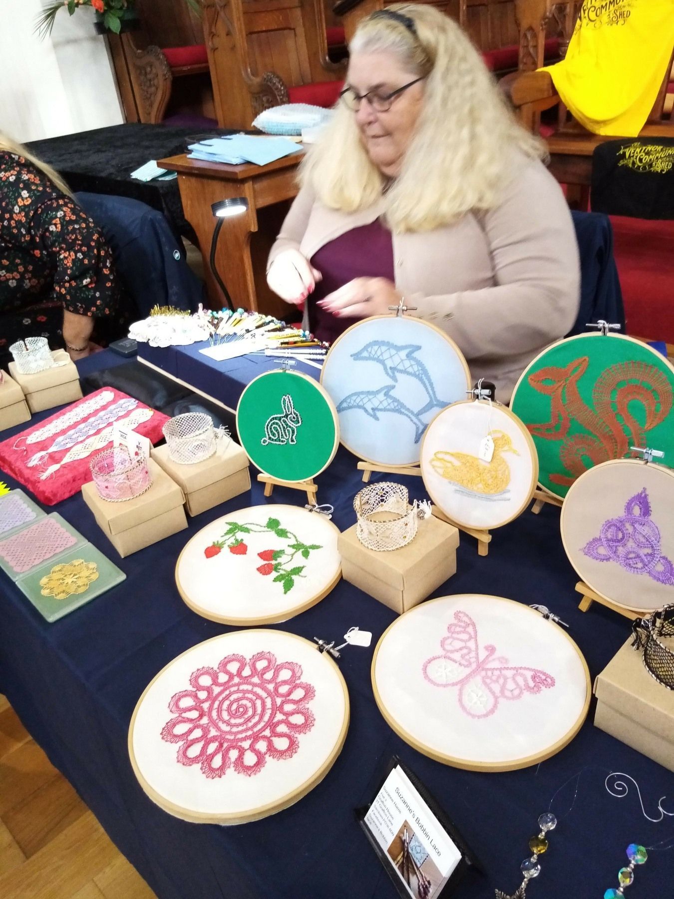 A woman is sitting at a table with embroidery hoops on it.