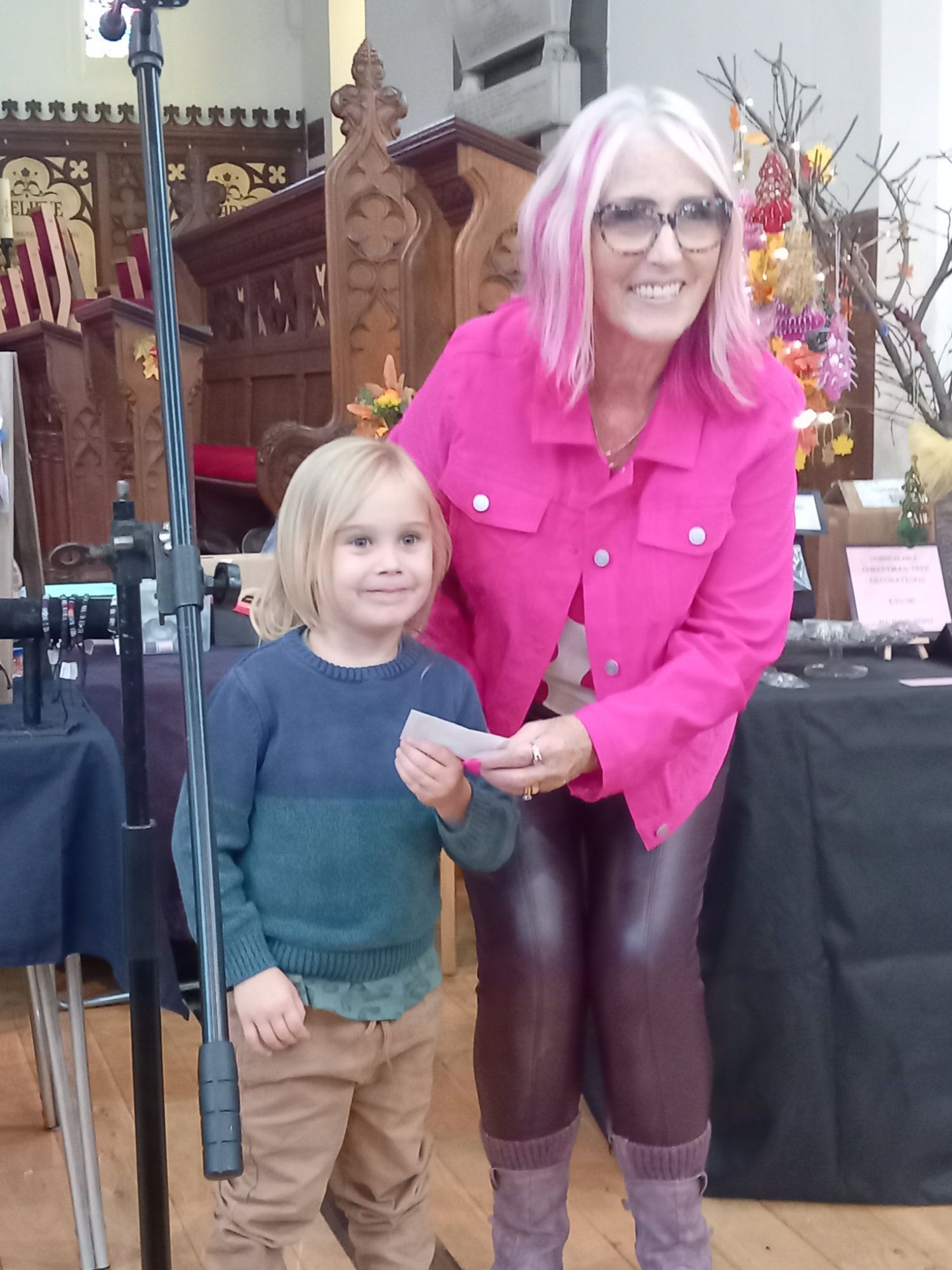 A woman with pink hair is standing next to a little boy holding a piece of paper.