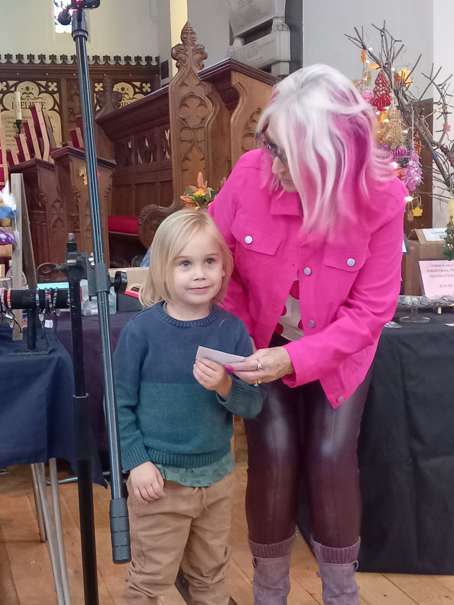 A woman in a pink jacket is standing next to a little boy holding a piece of paper.
