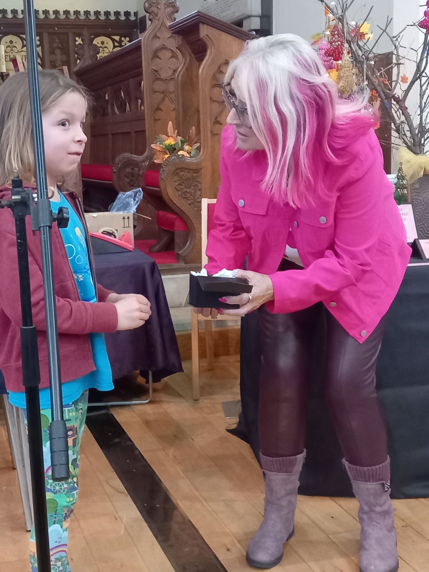 A woman with pink hair is giving a gift to a little girl
