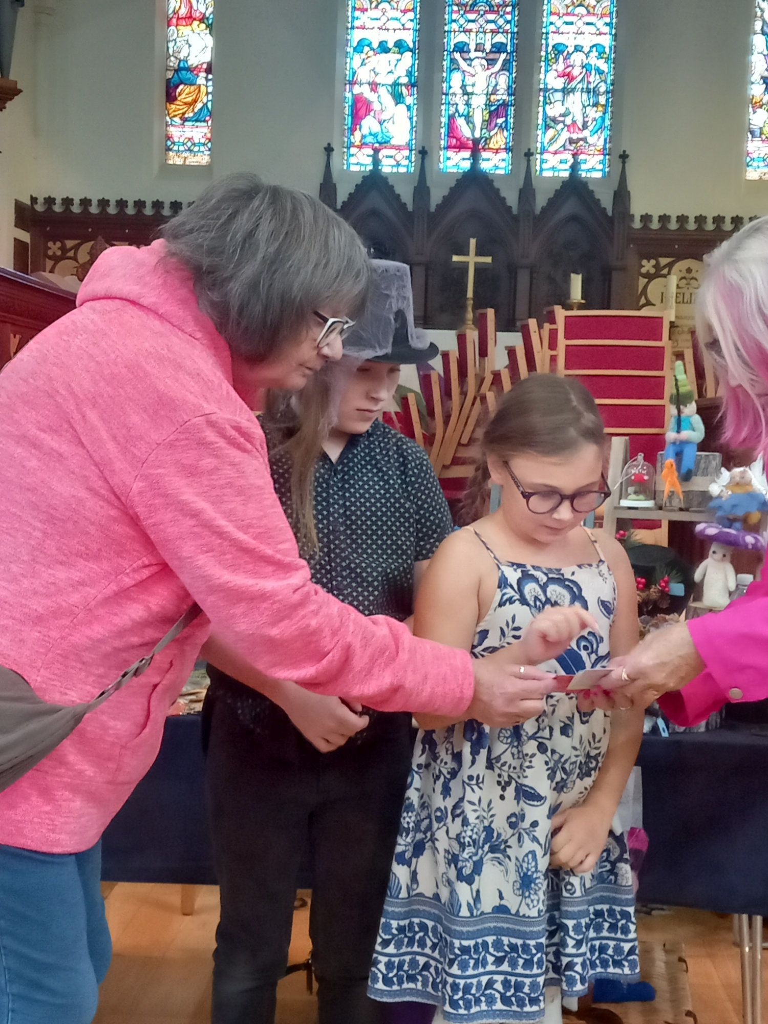 A woman in a pink sweatshirt is giving a girl a gift in a church