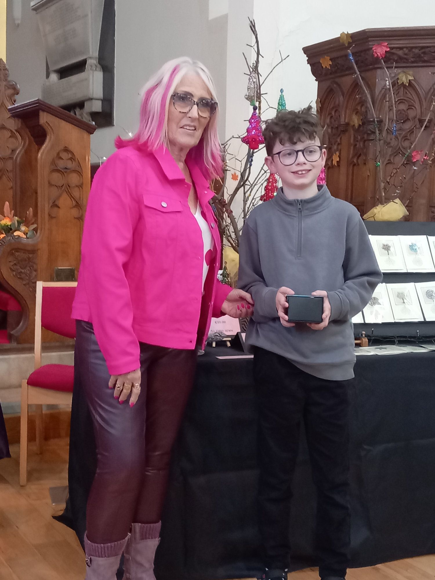 A woman in a pink jacket is standing next to a boy in a gray sweater.