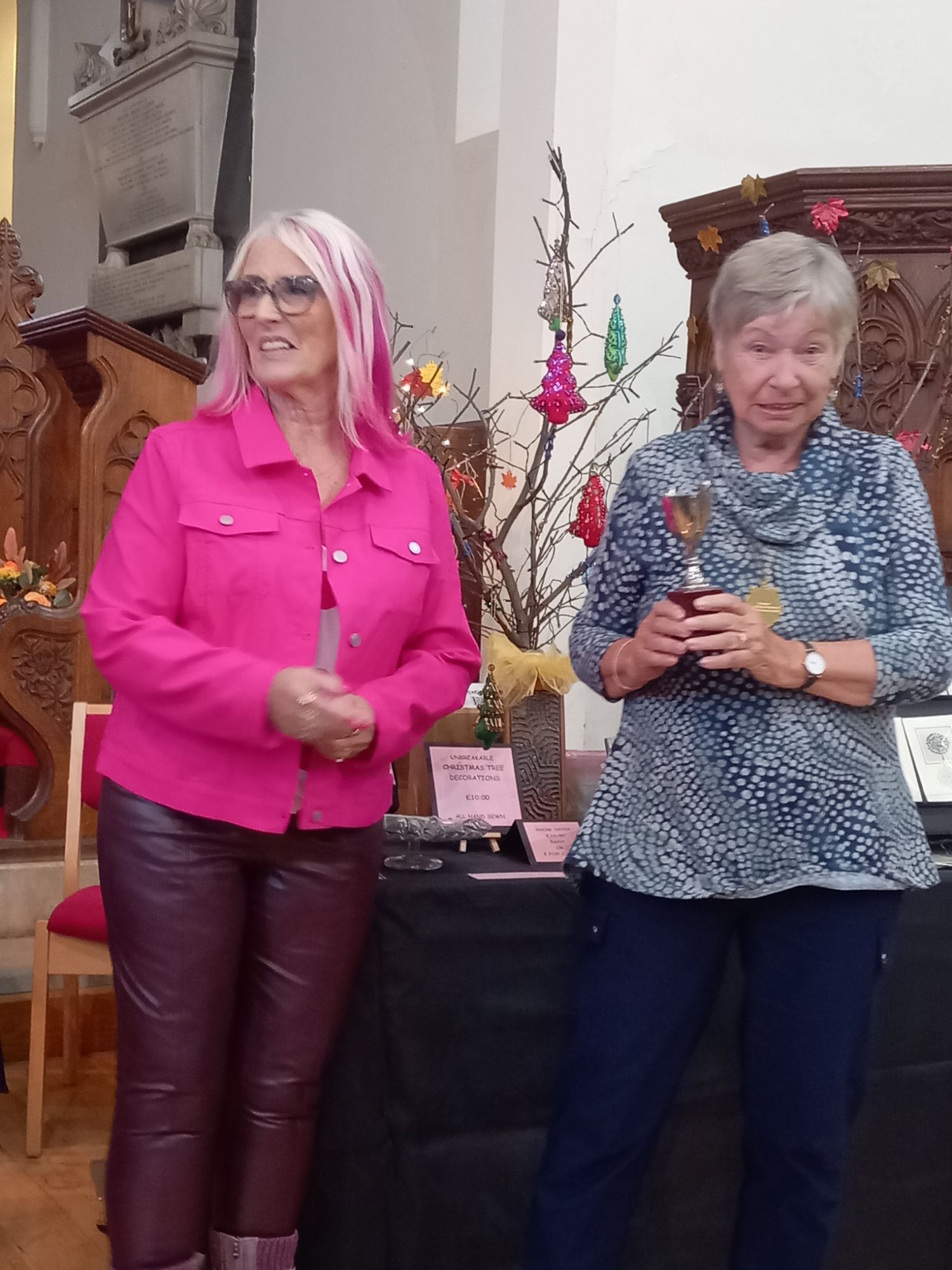 Two women are standing next to each other in a room holding trophies.