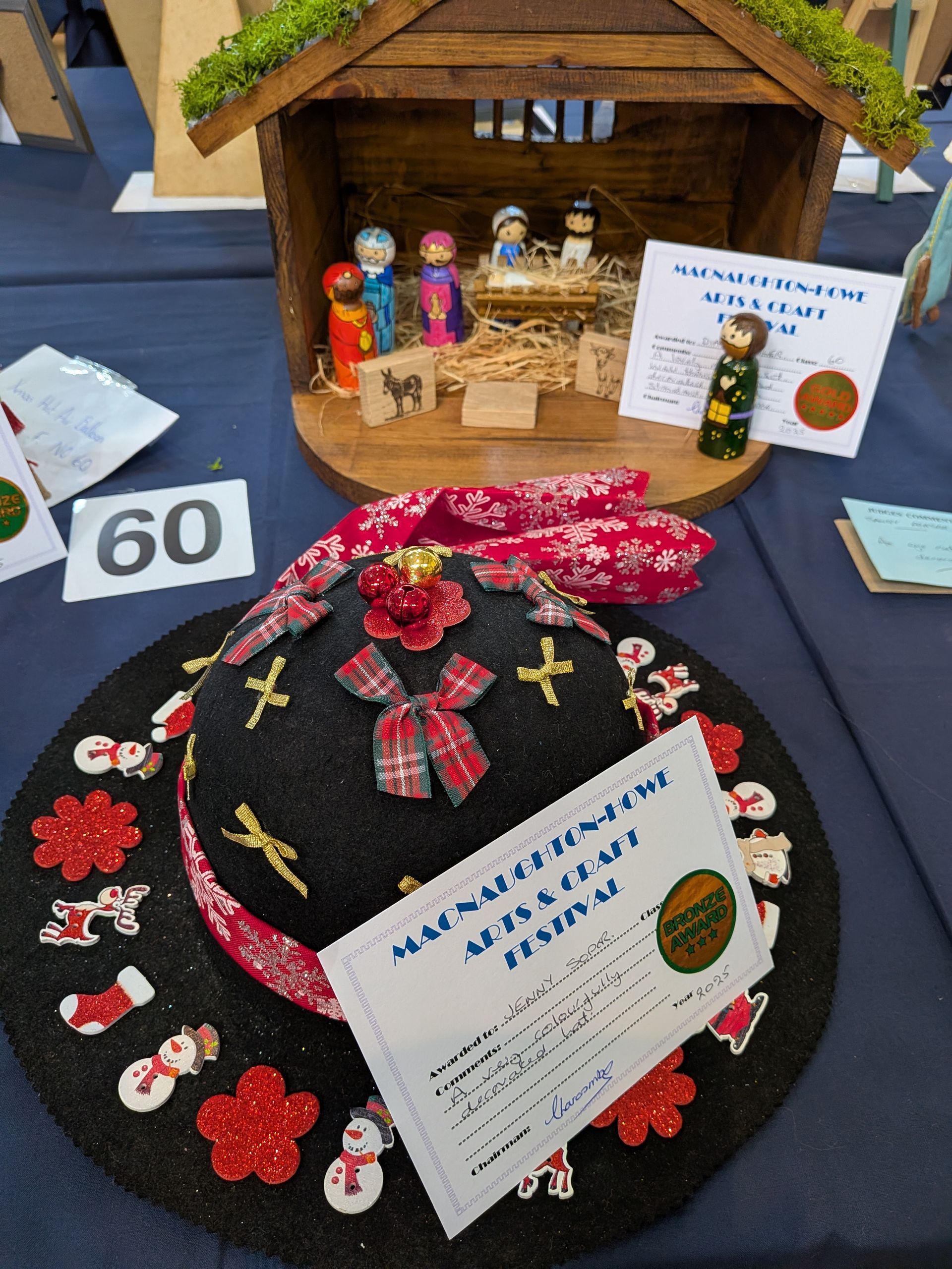 Nativity scene and decorated hat on a table, possibly at a craft fair, with a 