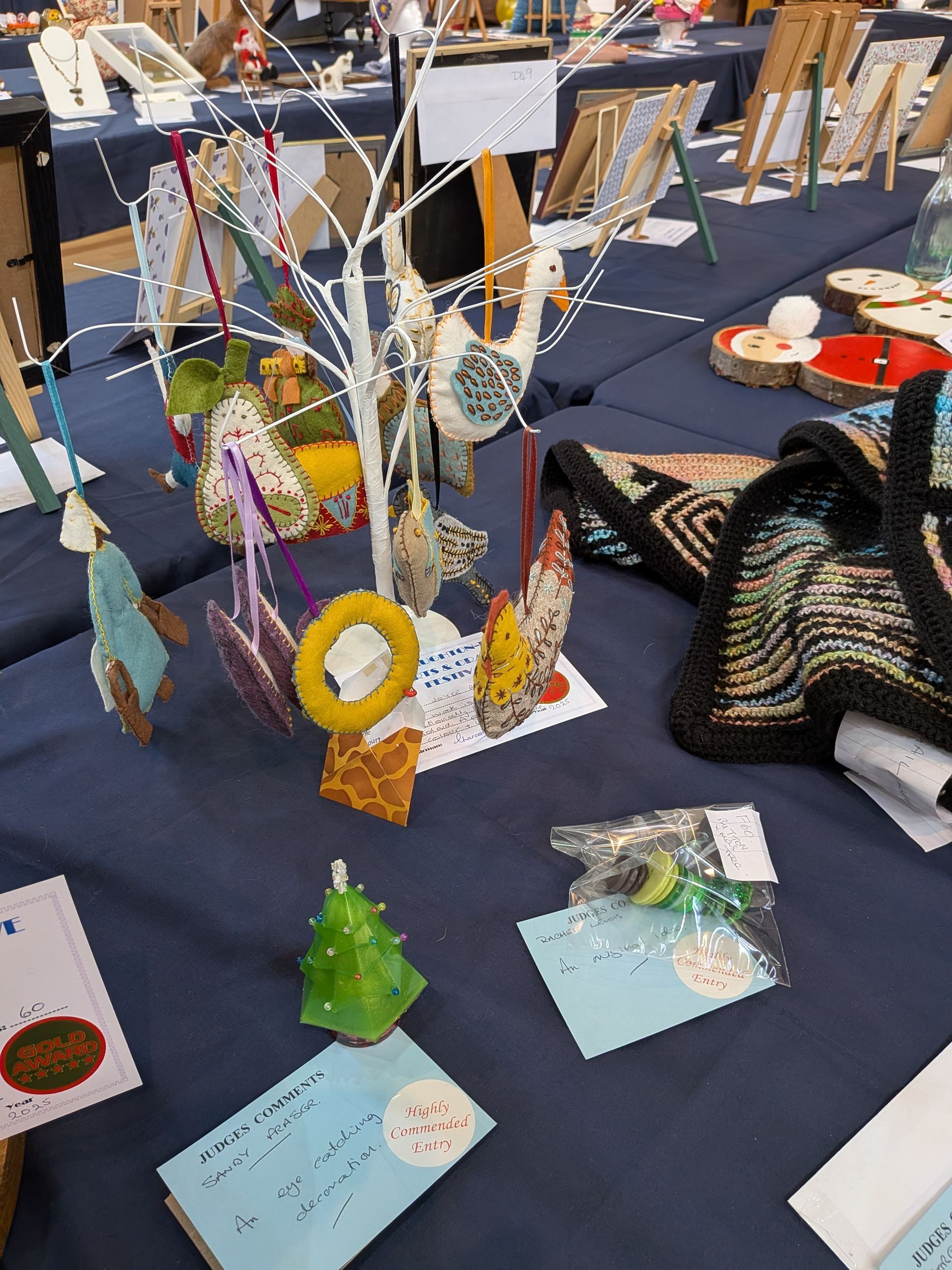 Table display with handmade ornaments, jewelry, and crafts at an indoor market, blue tablecloth.