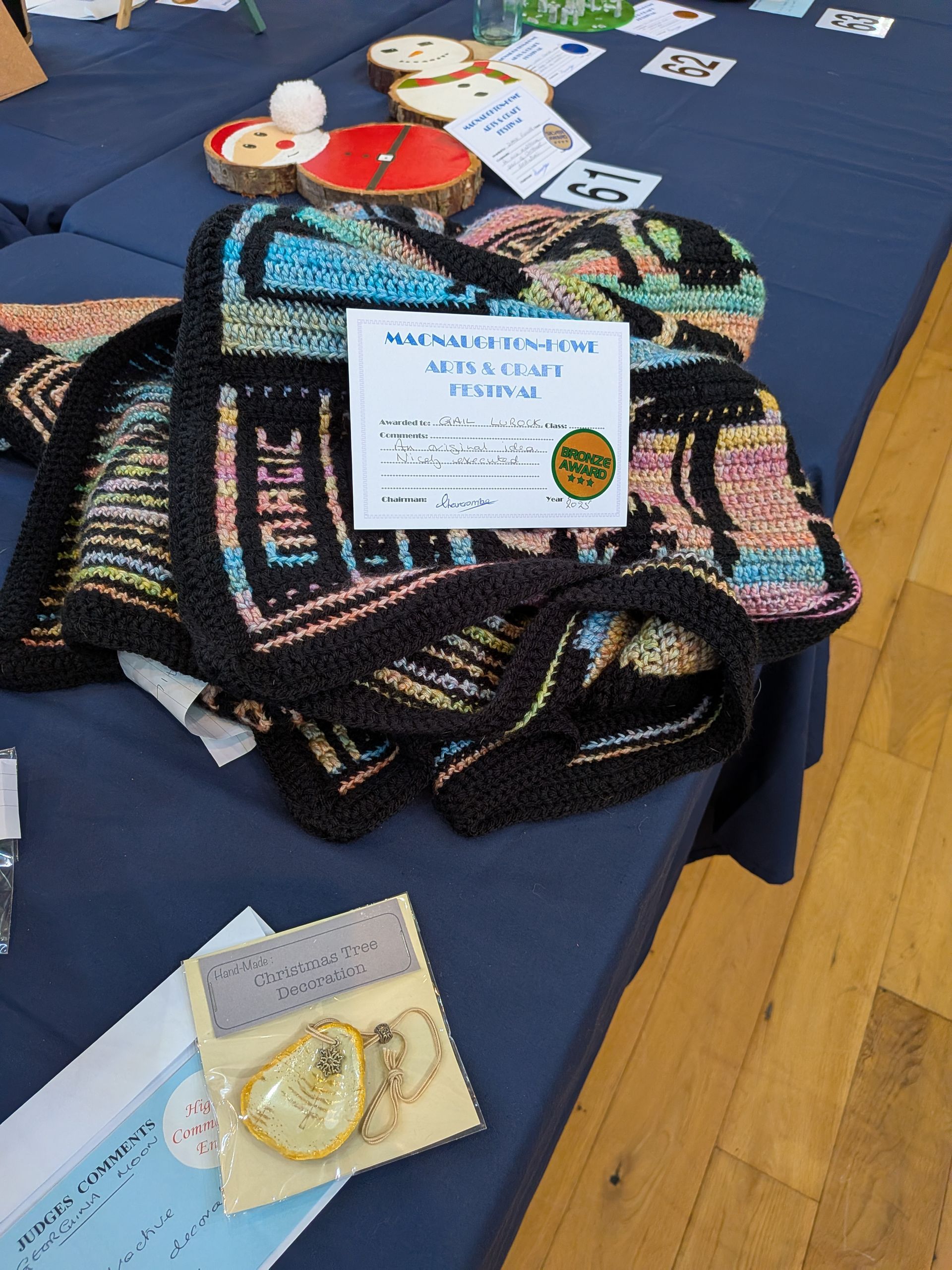 Knitted blanket with a prize certificate on a table at a craft fair.