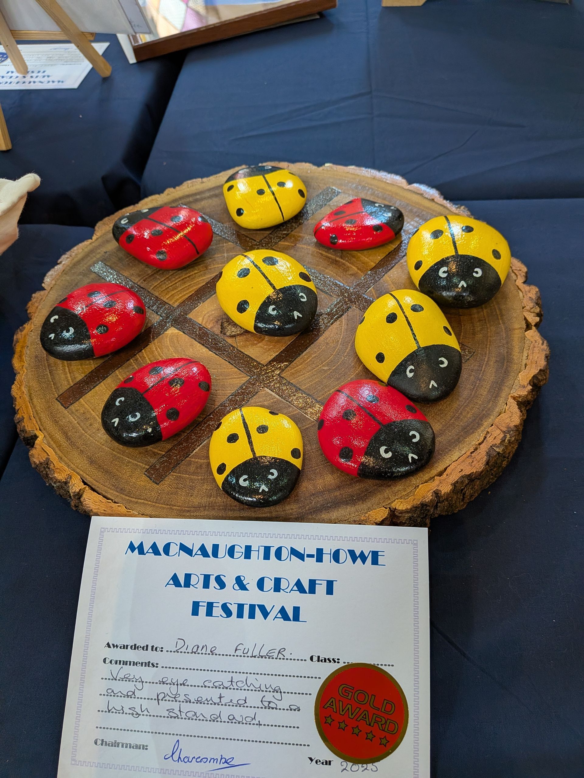 Tic-tac-toe game with ladybug-painted stones on a wooden round, displayed at an arts & craft festival.