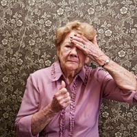 elderly woman wearing a pink shirt with her hand on forehead as if confused