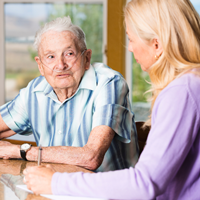 elderly man wearing a striped shirt talking to a woman with blonde hair wearing a purple shirt