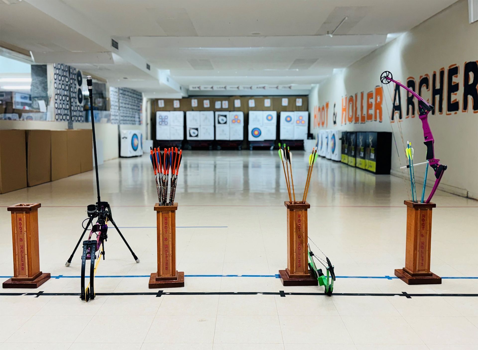 Archery range with target boards, bows on stands, and a shooting line in a bright indoor hall