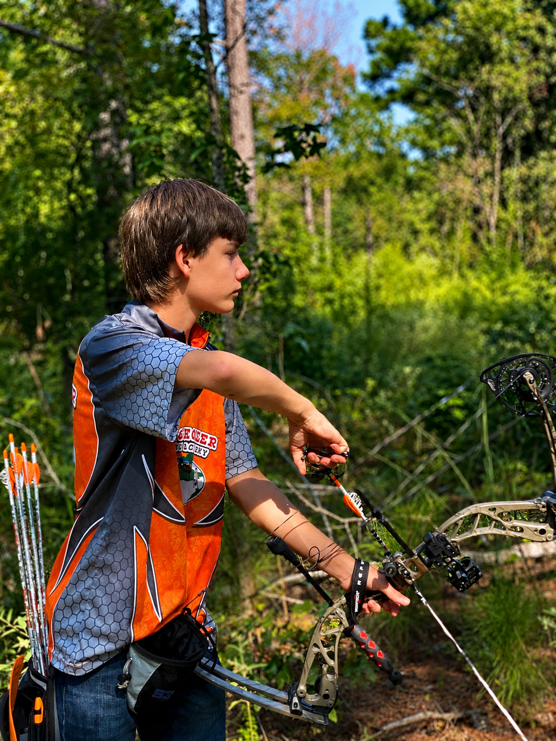 Person in an orange jersey stands by a bike, spraying water outdoors in a sunny green field.