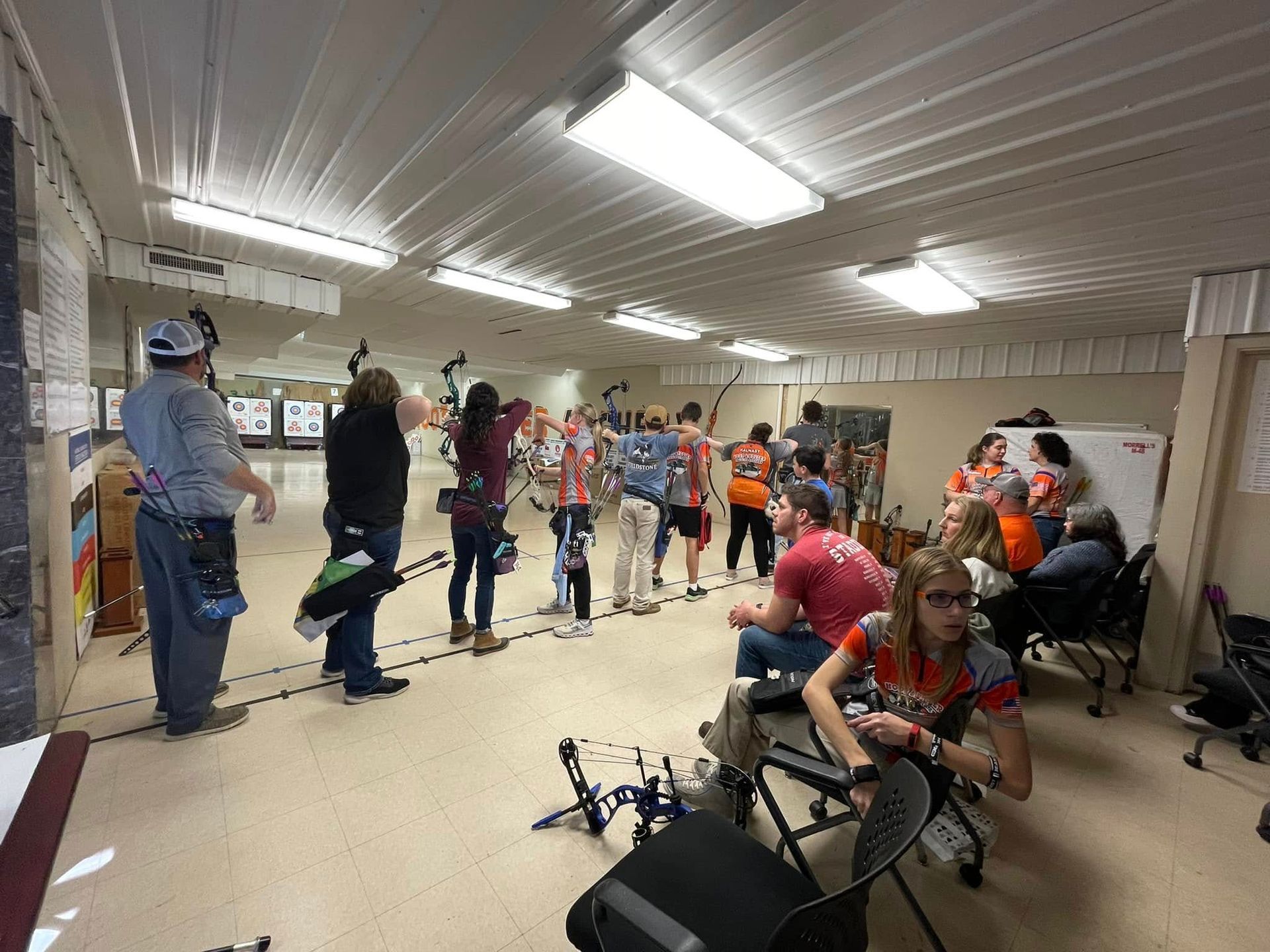 People with bows and arrows practicing archery indoors in a bright training room
