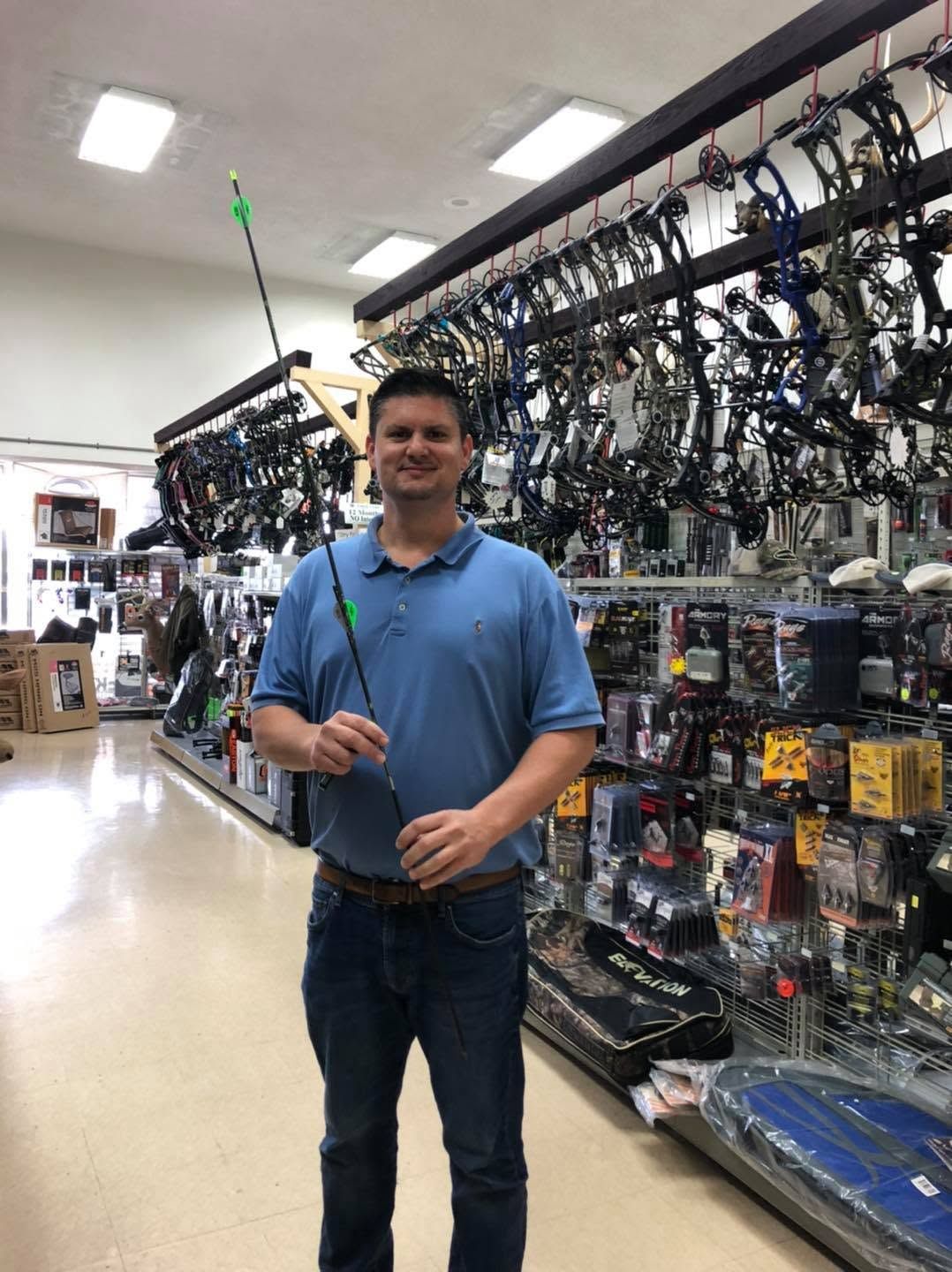 Person in a blue polo holding a fishing rod in an outdoor gear aisle.
