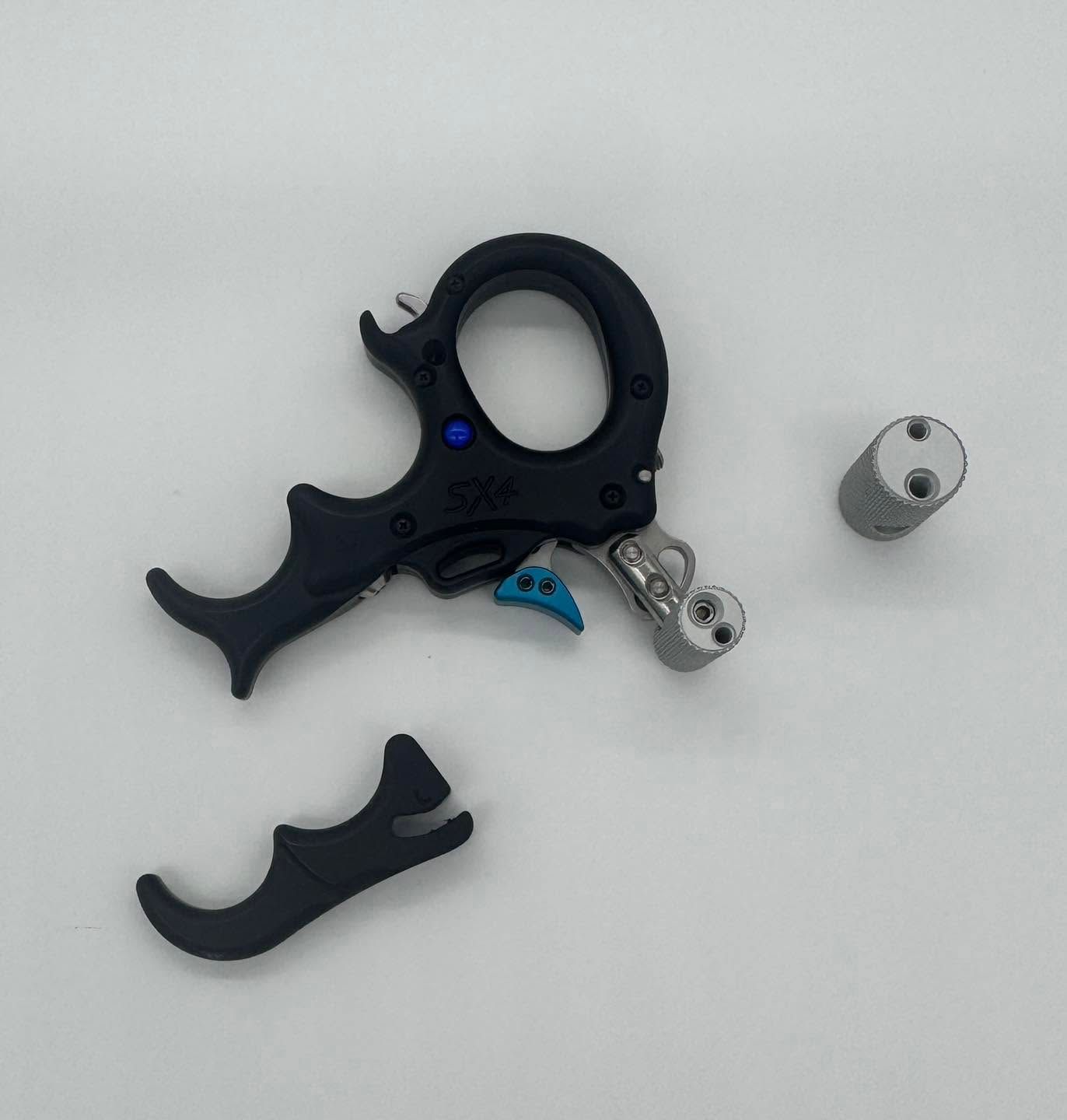 Black archery release aid with detachable parts and two small metal components on a light gray background