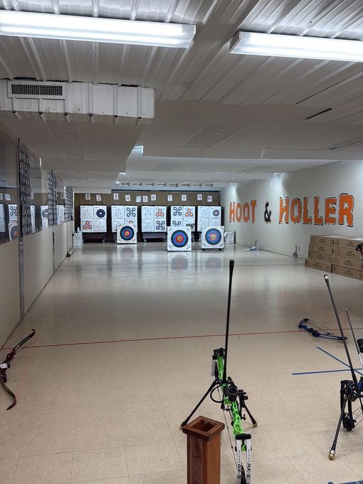 Indoor archery range with targets at the far end and bows set up in the foreground.