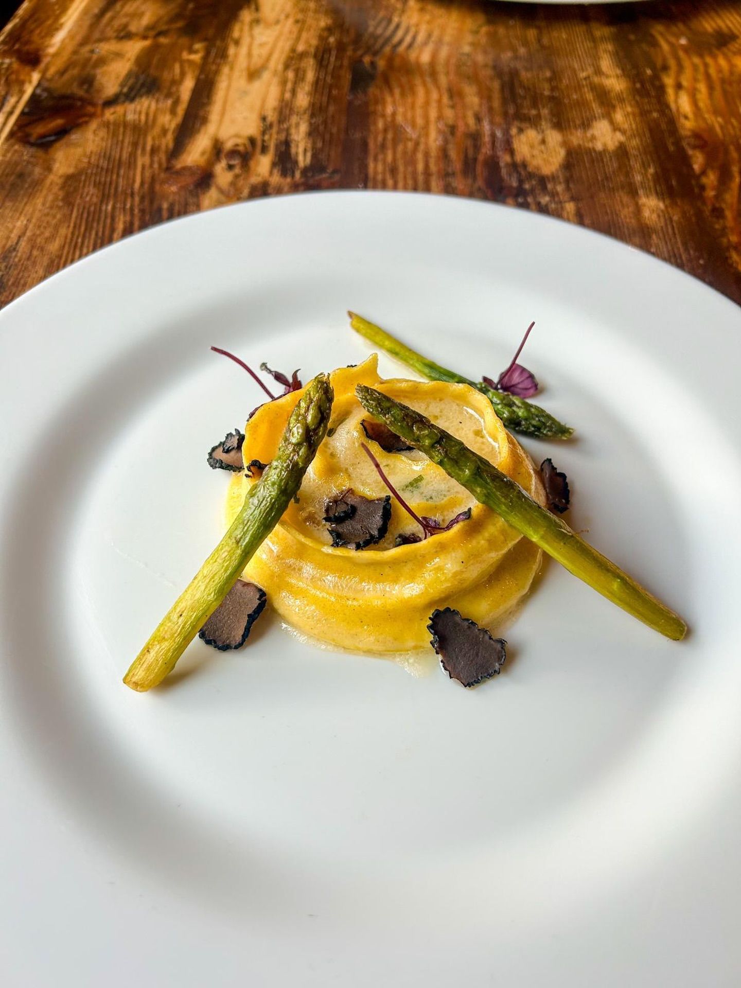 Piatto di pasta con punte di asparagi e fettine di tartufo su un piatto bianco.