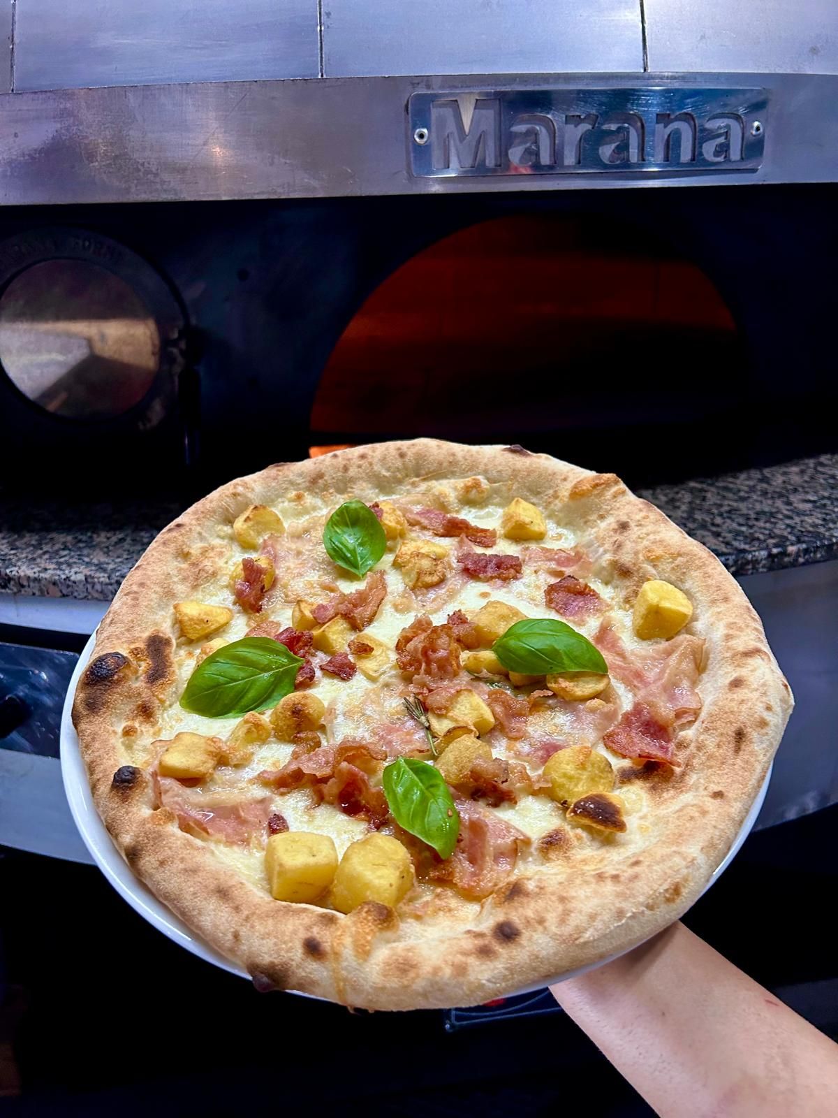 Pizza con condimenti, cotta davanti al forno a legna.