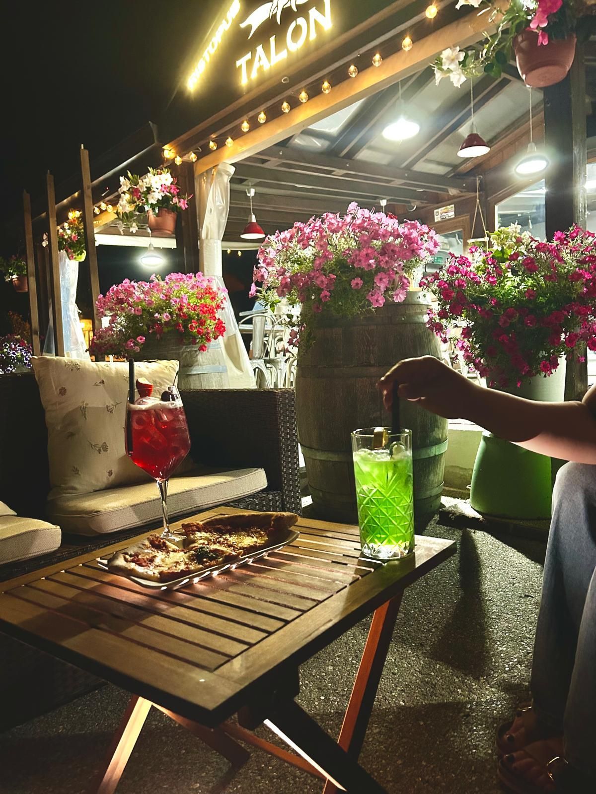 Area esterna con posti a sedere per la sera, cocktail, fiori e un'insegna del bar con la scritta