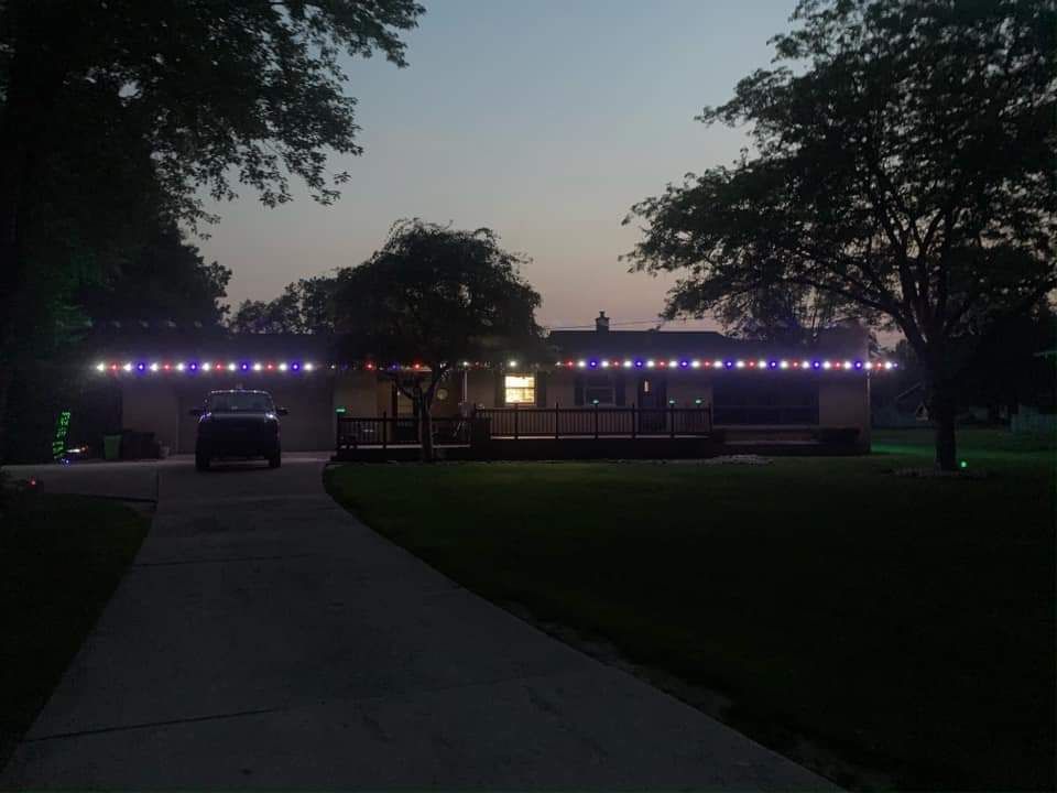 House exterior with string lights in blue and white, car parked in driveway at dusk.