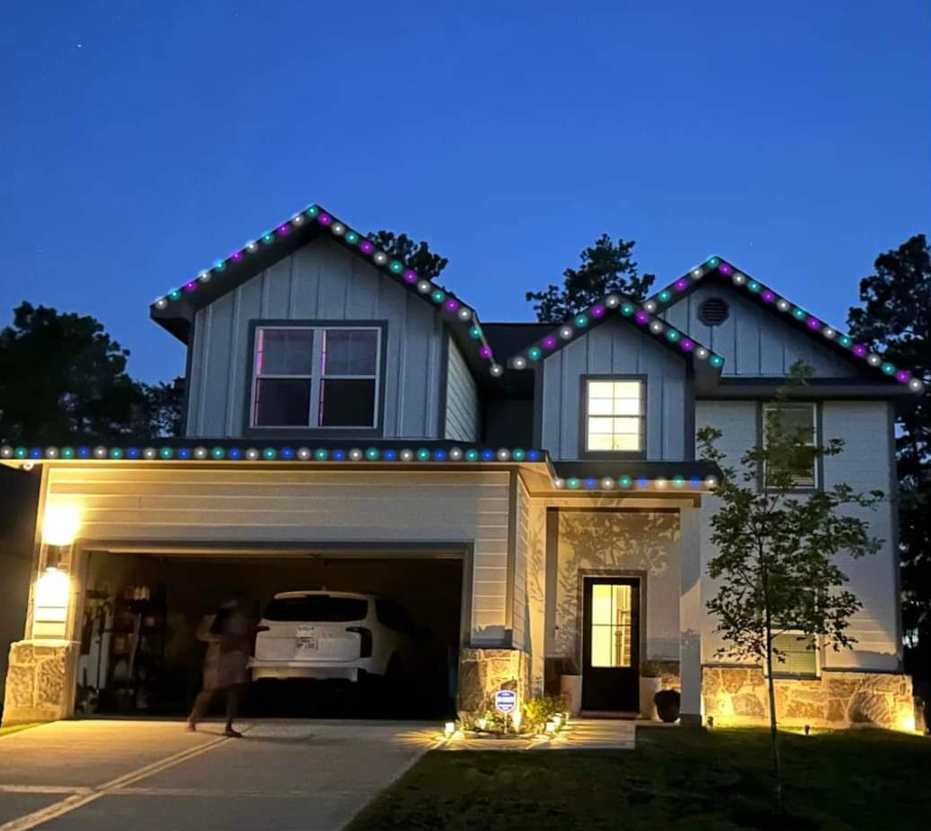 Two-story house at dusk with colorful Christmas lights. Person by the garage.