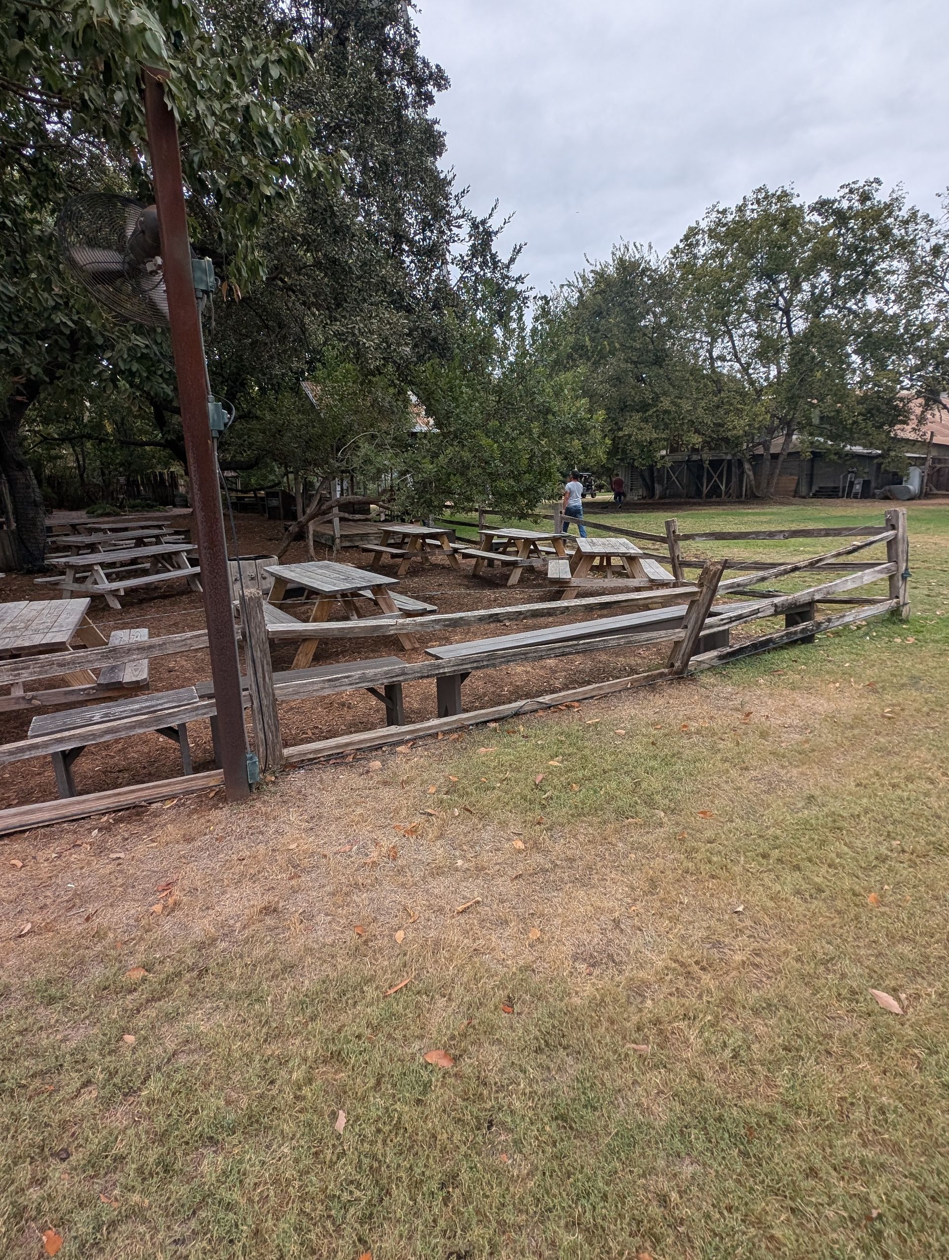 Foundation ruins enclosed by a wooden fence, with trees in the background and a cloudy sky overhead.