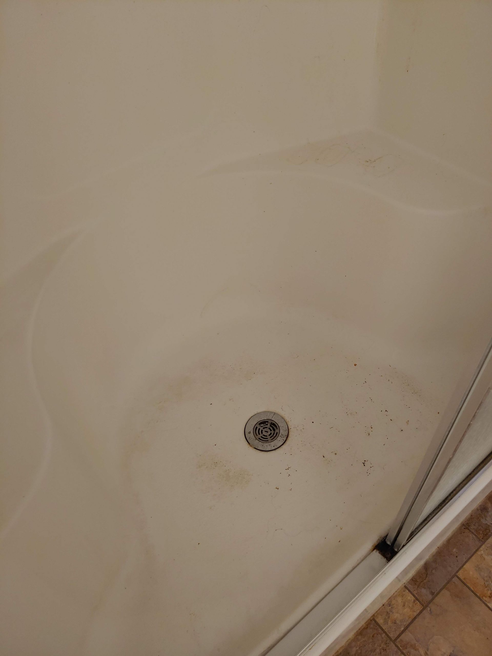 A close up of a dirty shower stall with a drain in it.
