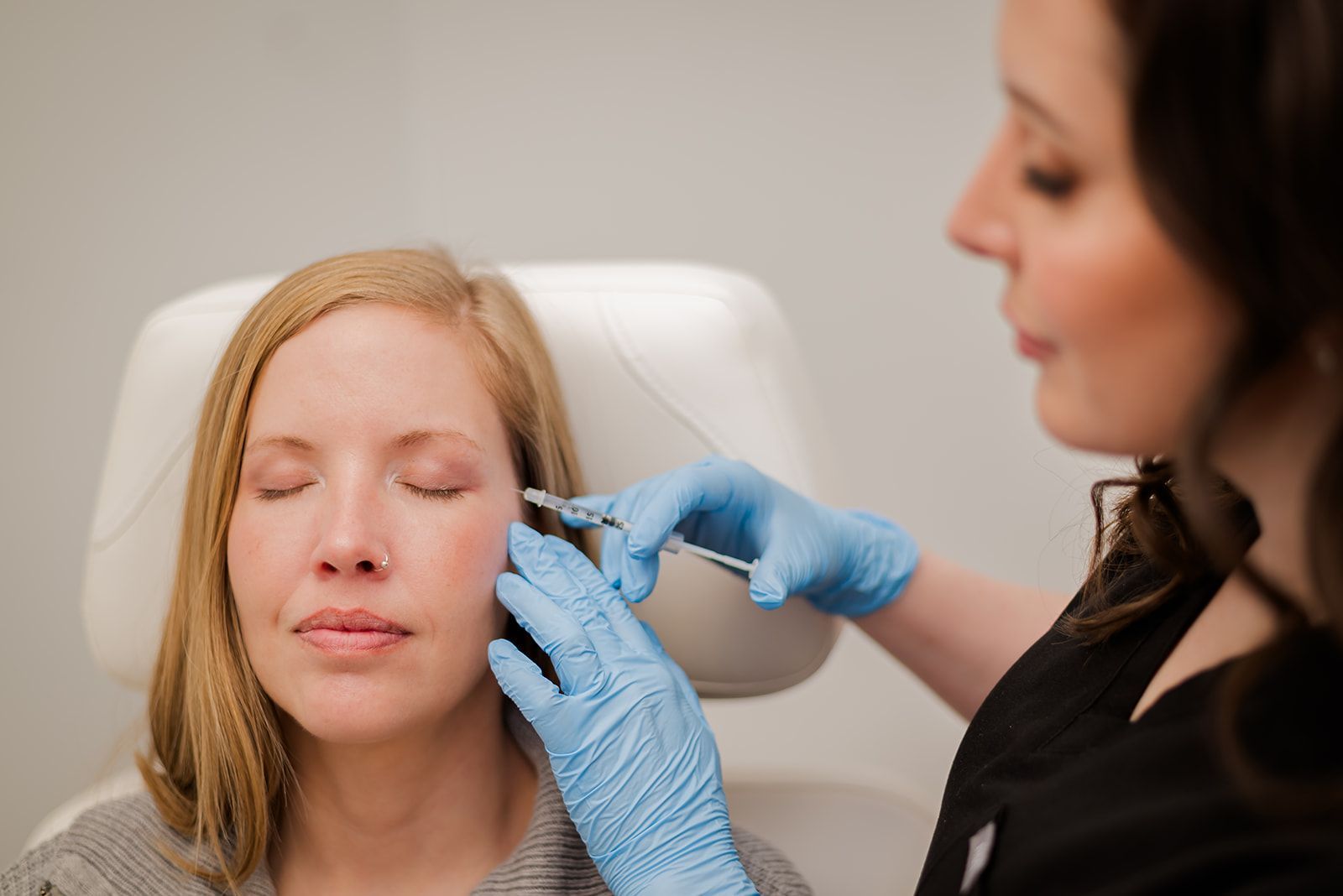 Nurse injector treating patient with cosmetic injections to the crow's feet area.