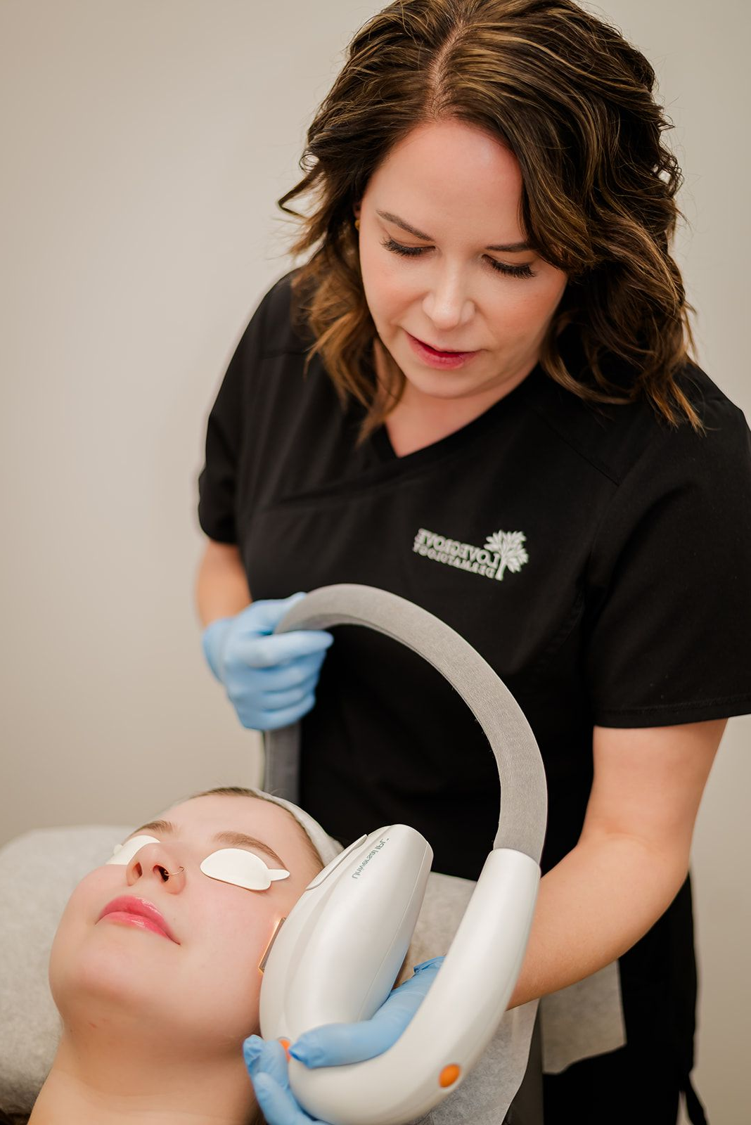 An aesthetician performs a facial procedure on a client; uses a device near the client's face.