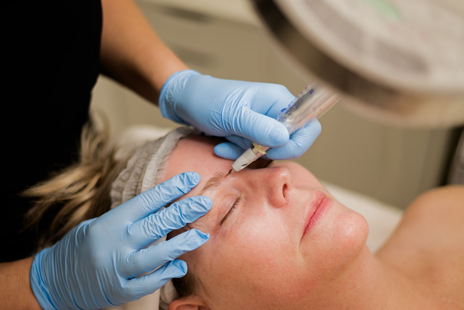 Woman receiving an eyebrow cosmetic procedure, performed by gloved hands. 
