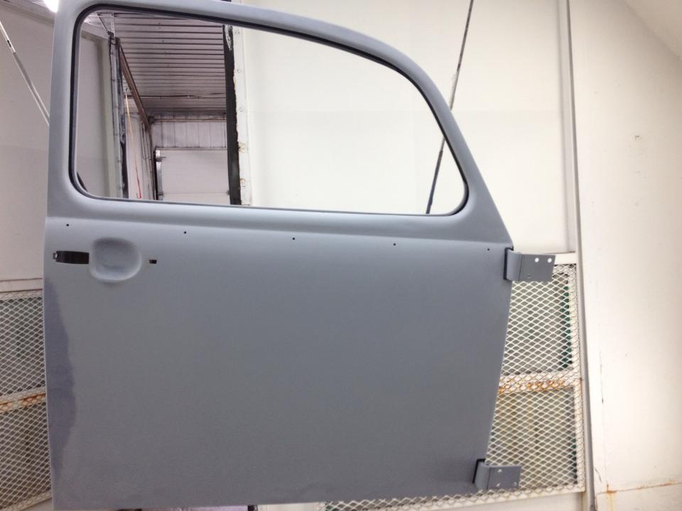 Coque de portière de voiture grise dans un atelier, vue de côté avec le cadre de la vitre et les charnières visibles.