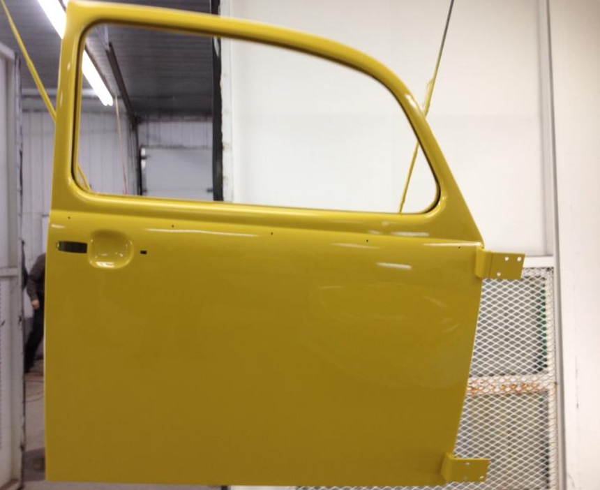 Panneau de portière jaune dans un atelier, vu de côté, avec le cadre de la vitre et la poignée visibles.
